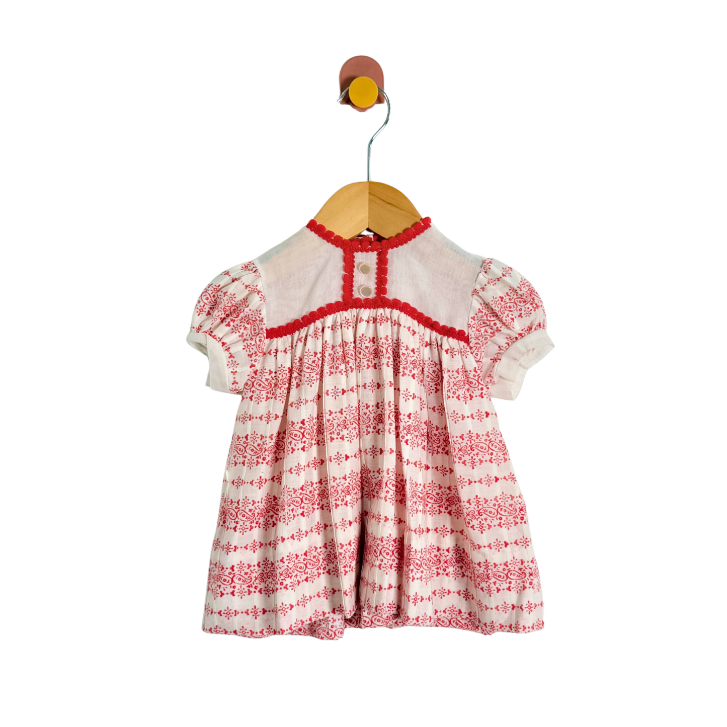 Red and white patterned dress on a wooden hanger against a white background