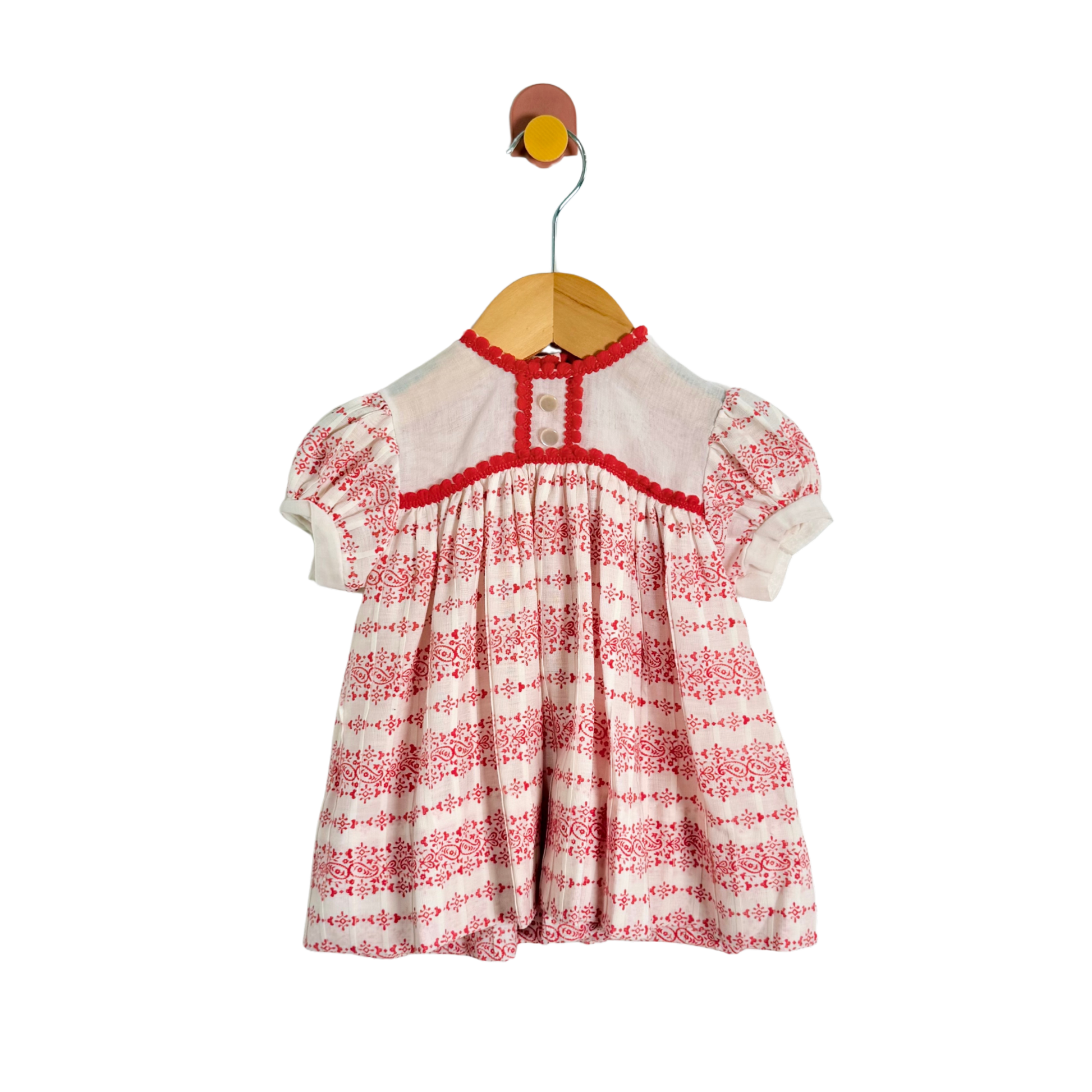 Red and white patterned dress on a wooden hanger against a white background