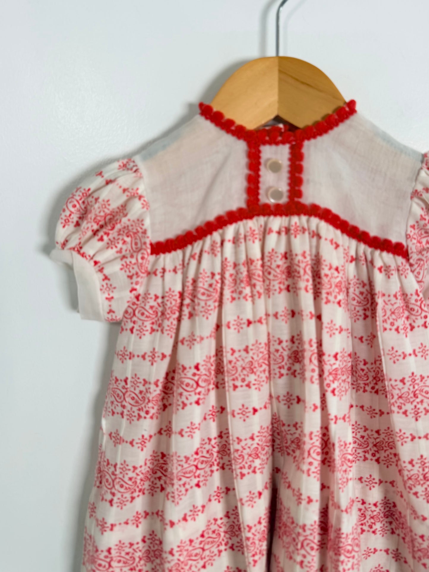 White dress with red floral pattern on a hanger against a white background