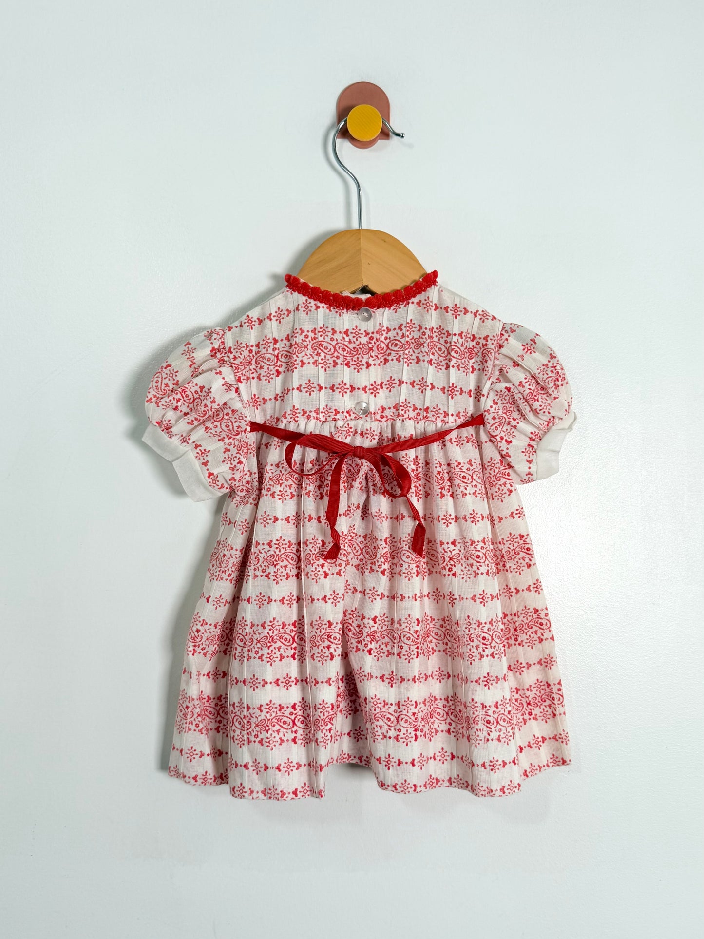 Red and white floral dress on a wooden hanger against a light gray background