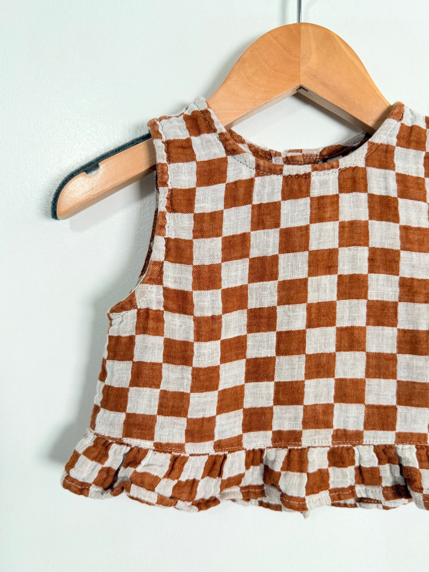 Brown and white checkered top on a wooden hanger against a light background