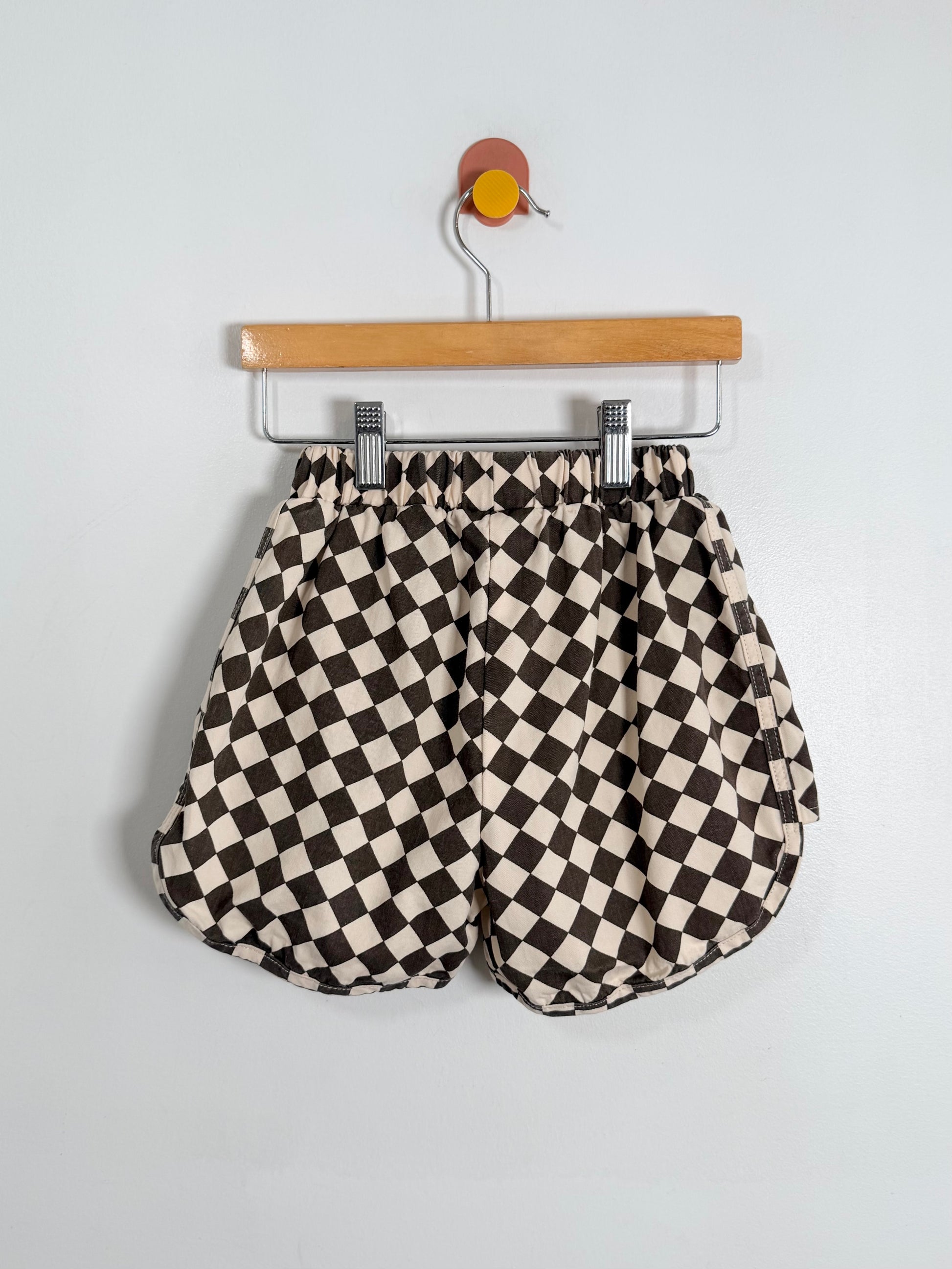 Black and white checkered shorts on a hanger against a light gray background