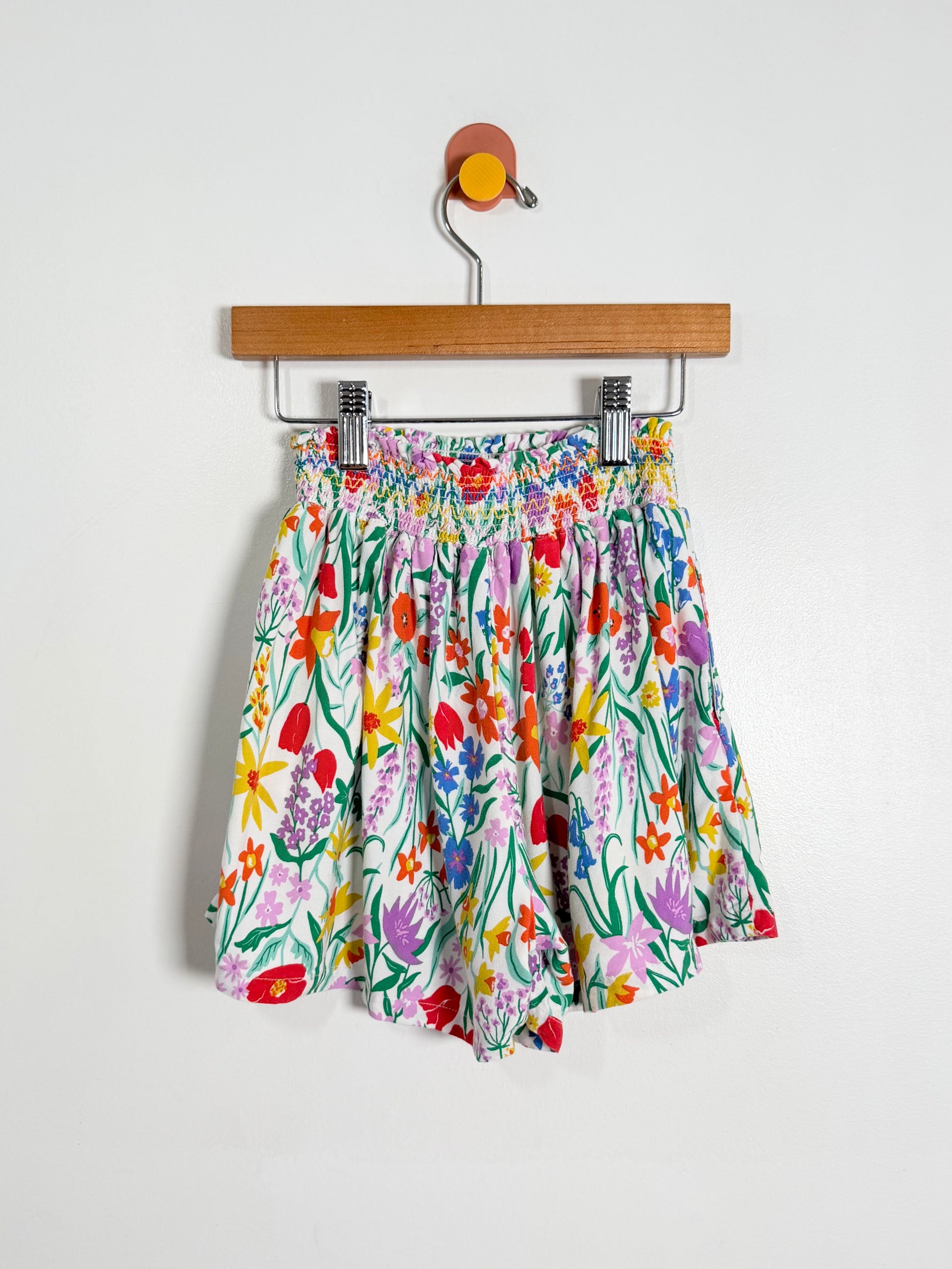 Colorful floral shorts on a wooden hanger against a white background