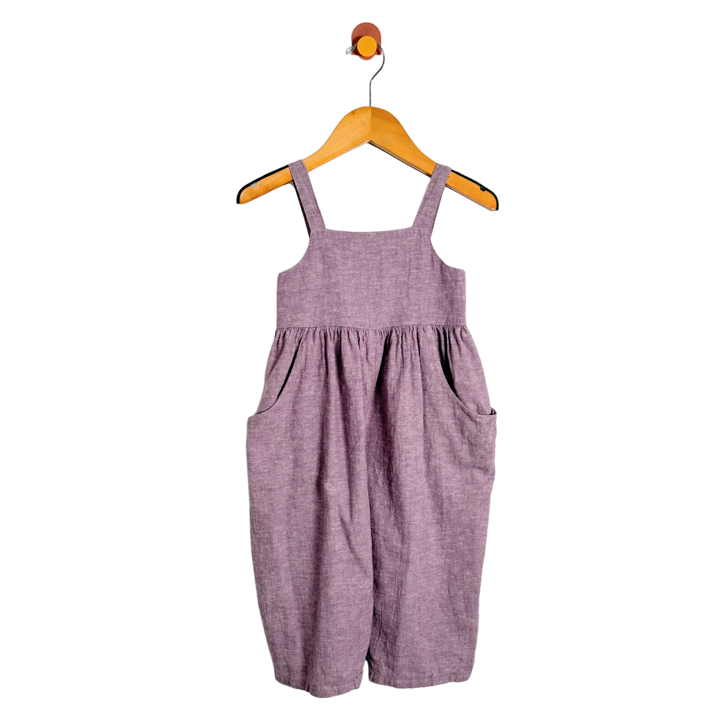 Purple overalls hanging on a wooden hanger against a white background