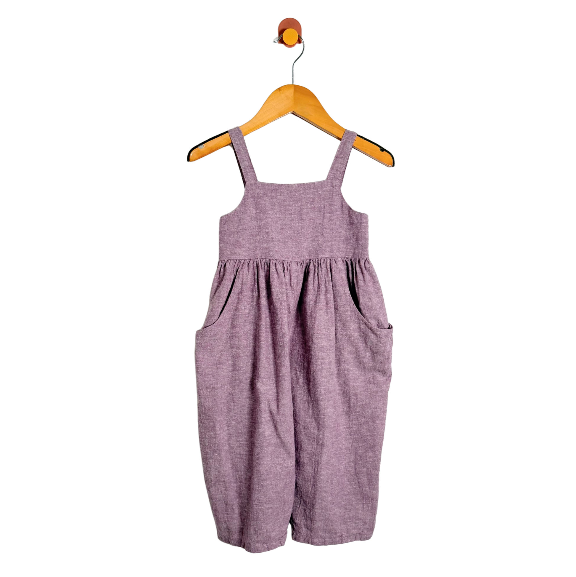 Purple overalls hanging on a wooden hanger against a white background