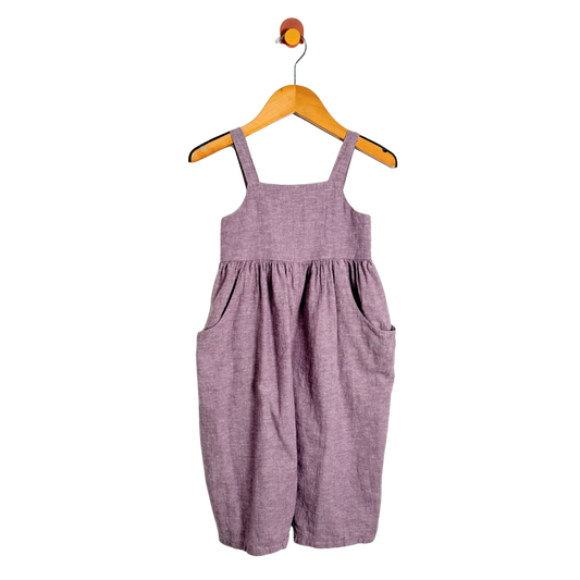 Purple overalls hanging on a wooden hanger against a white background