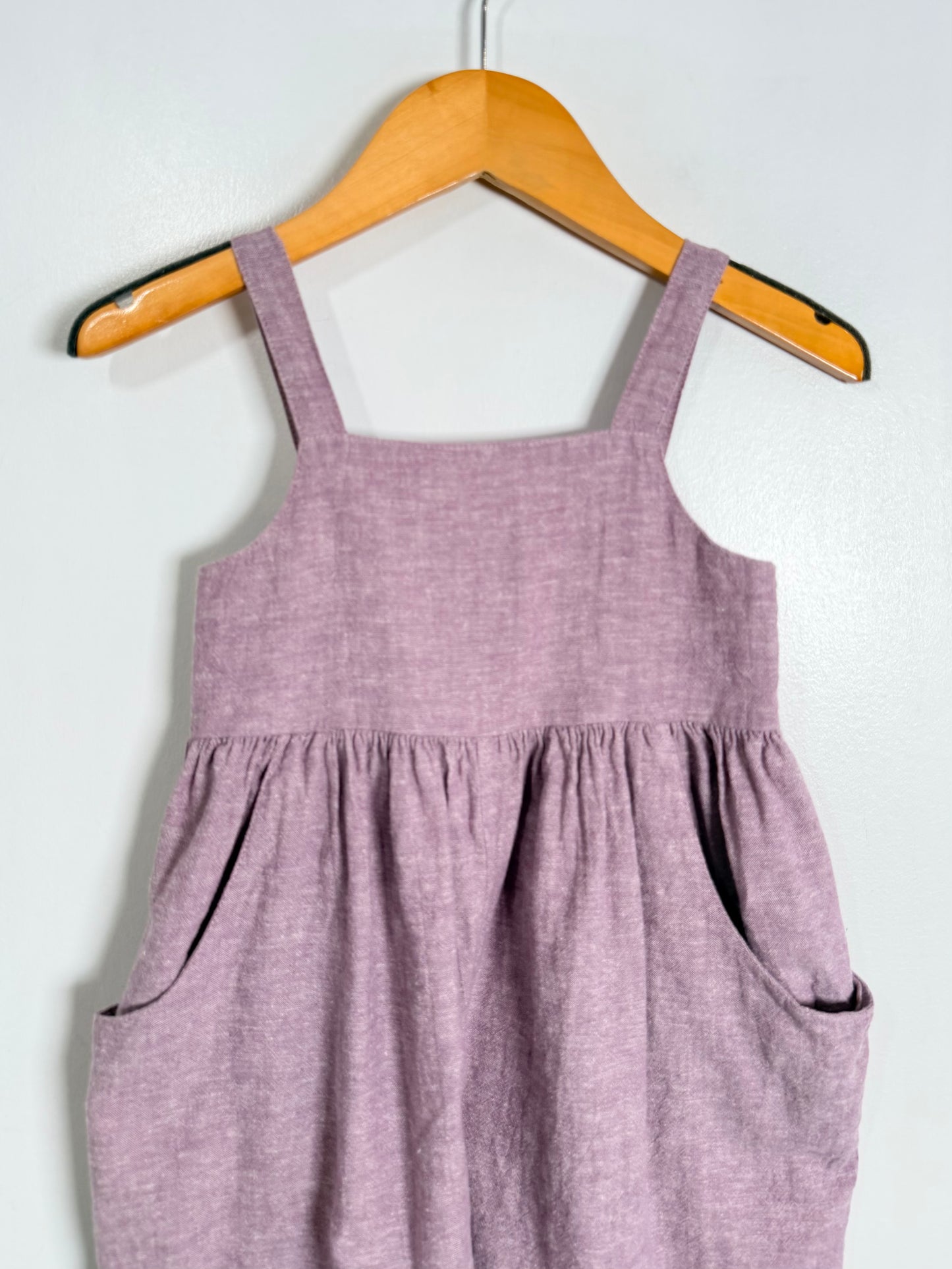Purple jumpsuit on a wooden hanger against a white background