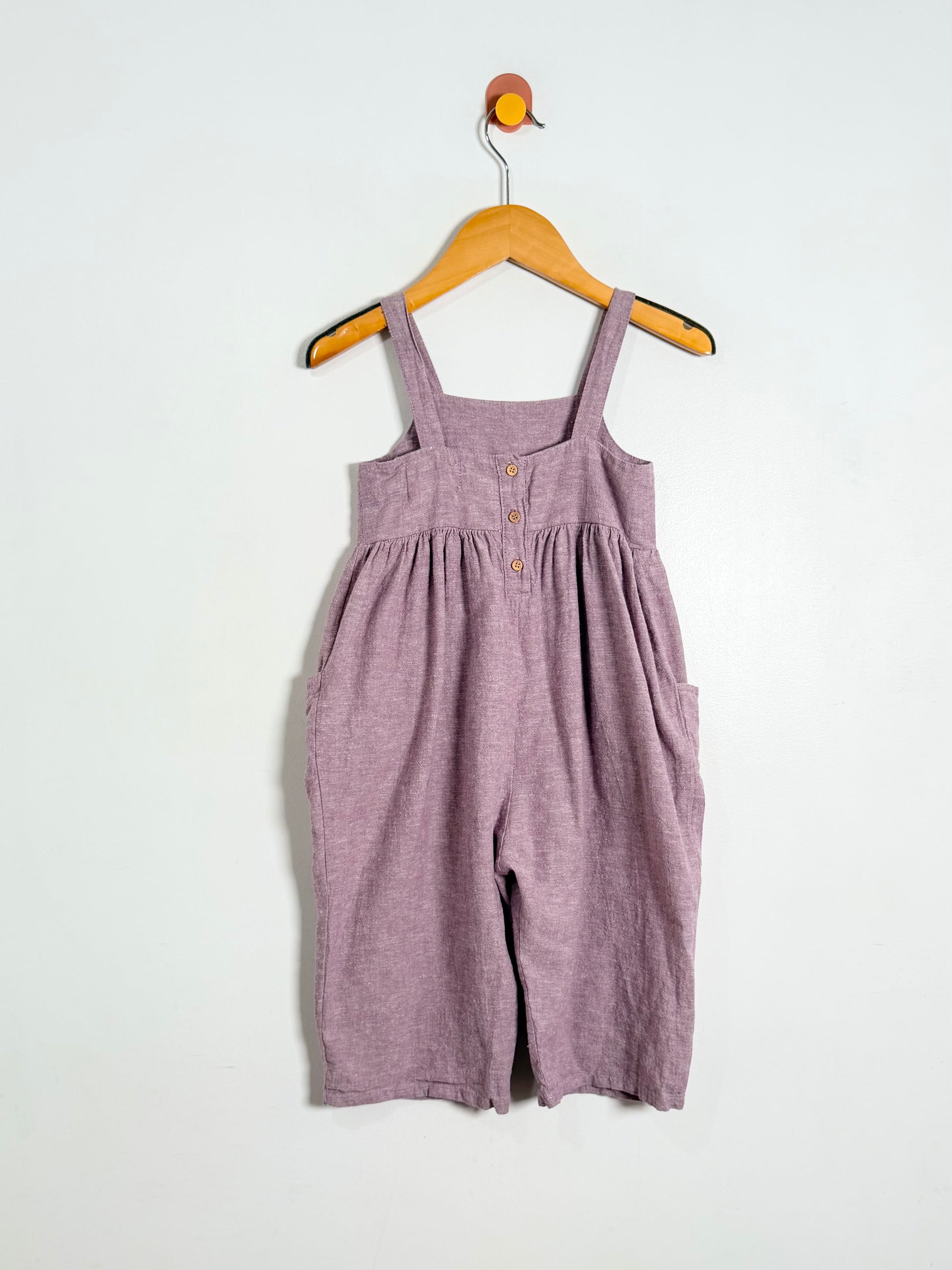 Purple overalls hanging on a wooden hanger against a white background