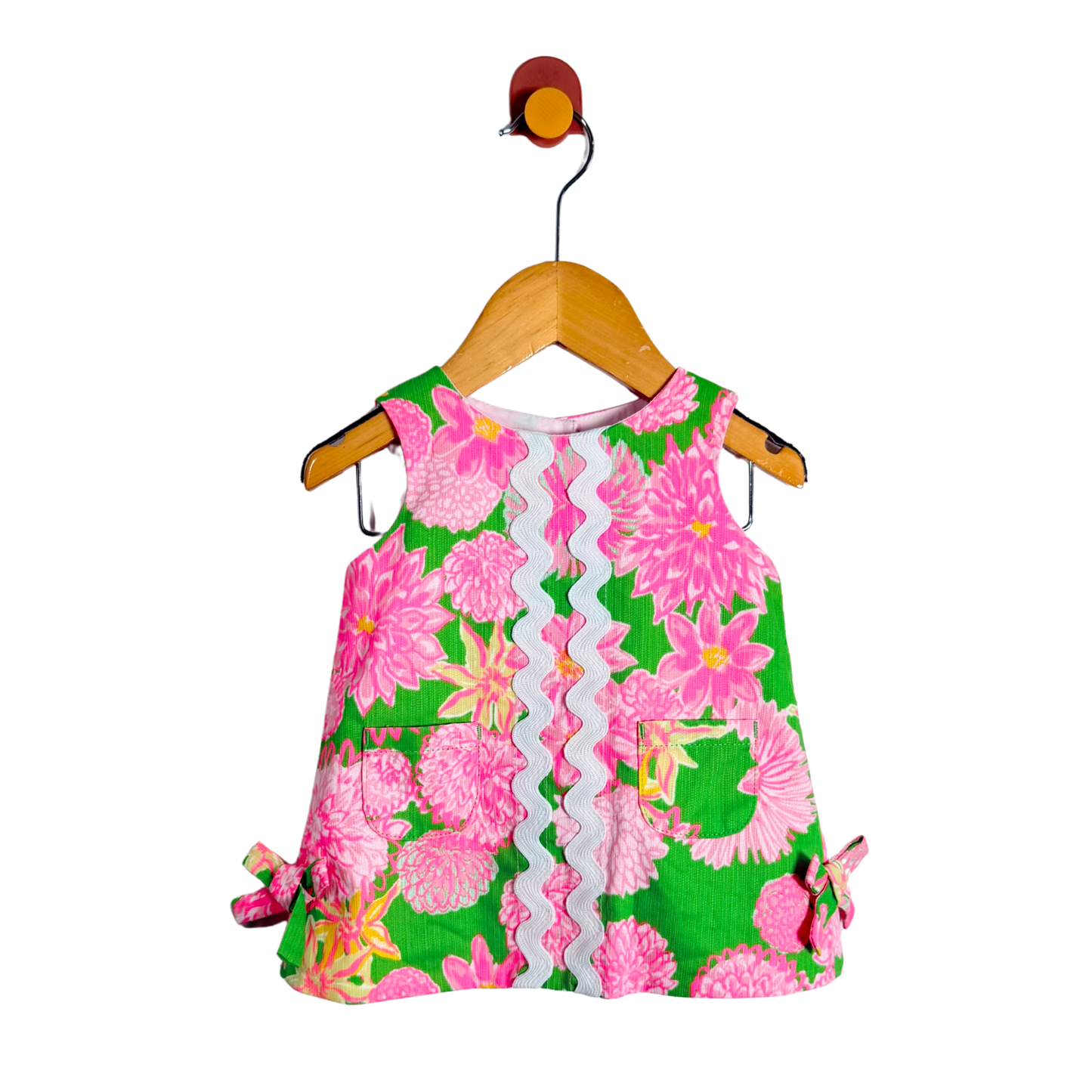 Floral dress with pink flowers on a green background, hanging on a wooden hanger against a white background.