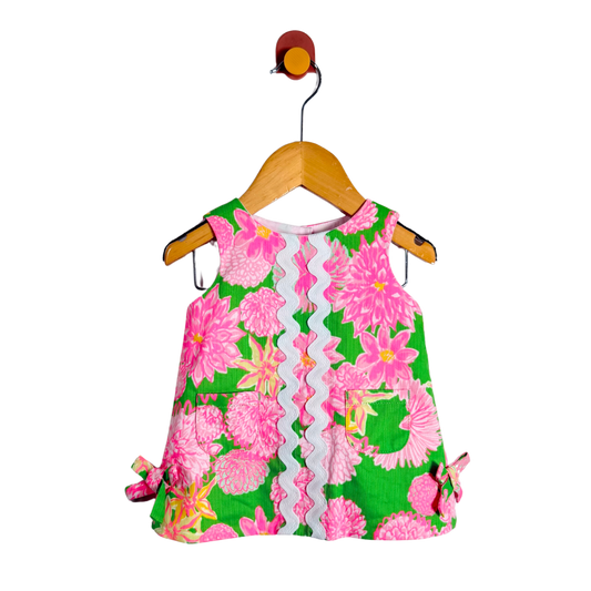 Floral dress with pink flowers on a green background, hanging on a wooden hanger against a white background.