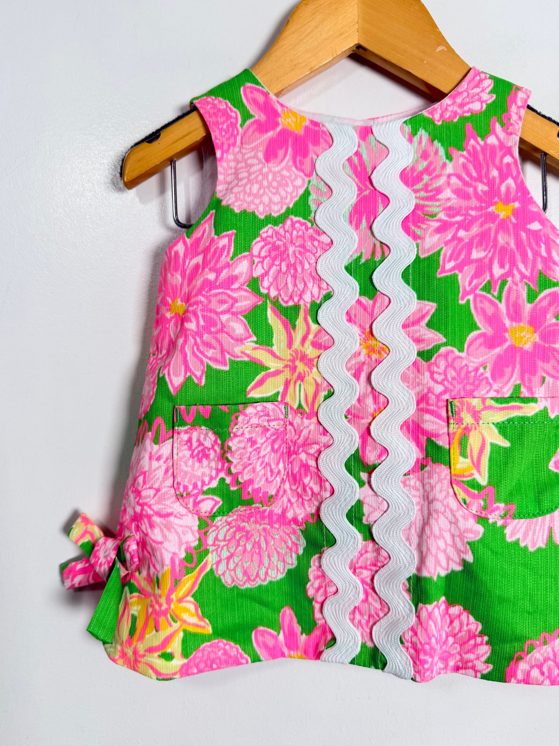 Children's dress with pink floral pattern on a hanger against a white background