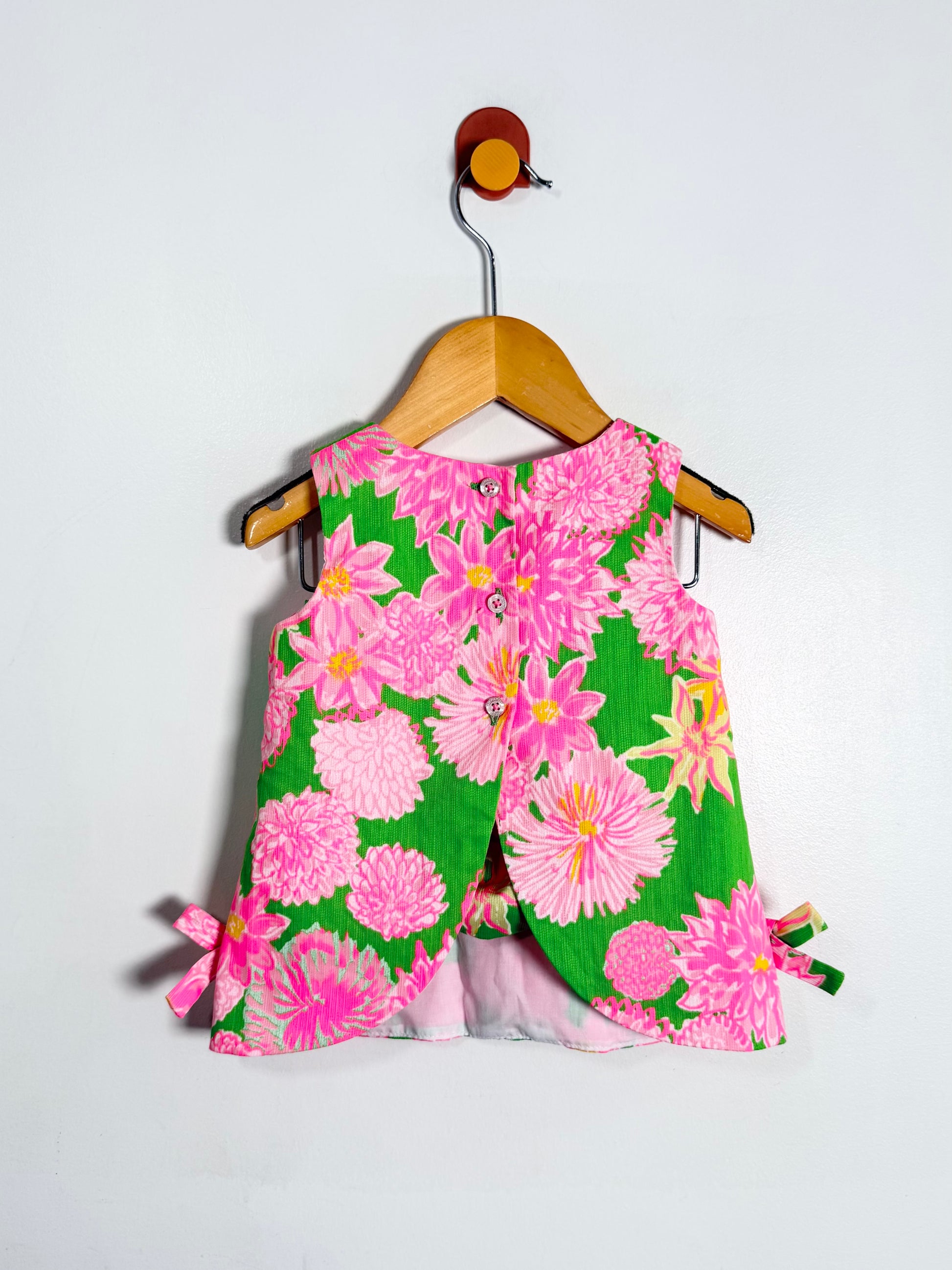 Floral dress with pink and green flowers on a hanger against a white background