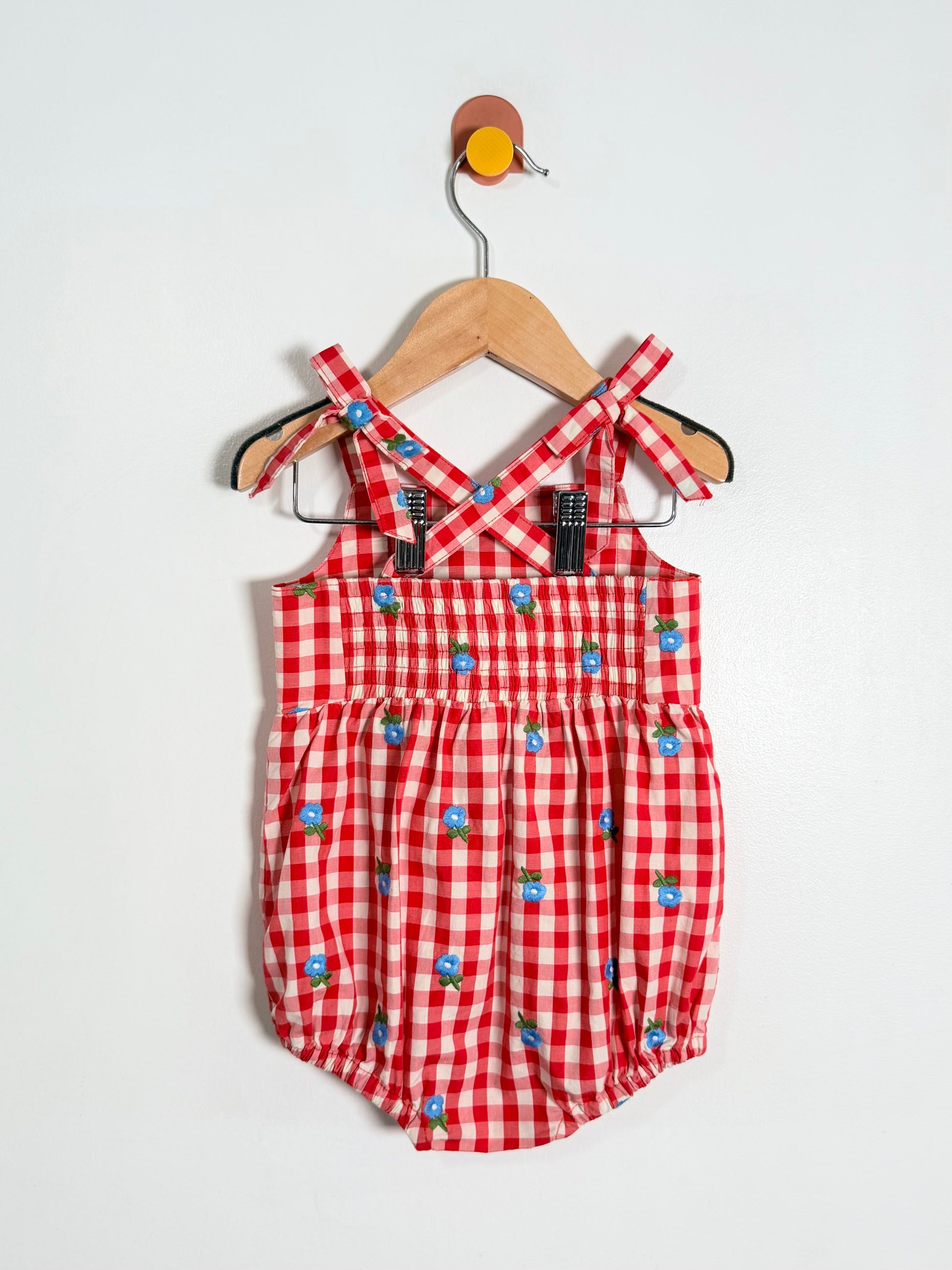 Red checkered romper with blue floral patterns on a hanger against a white background