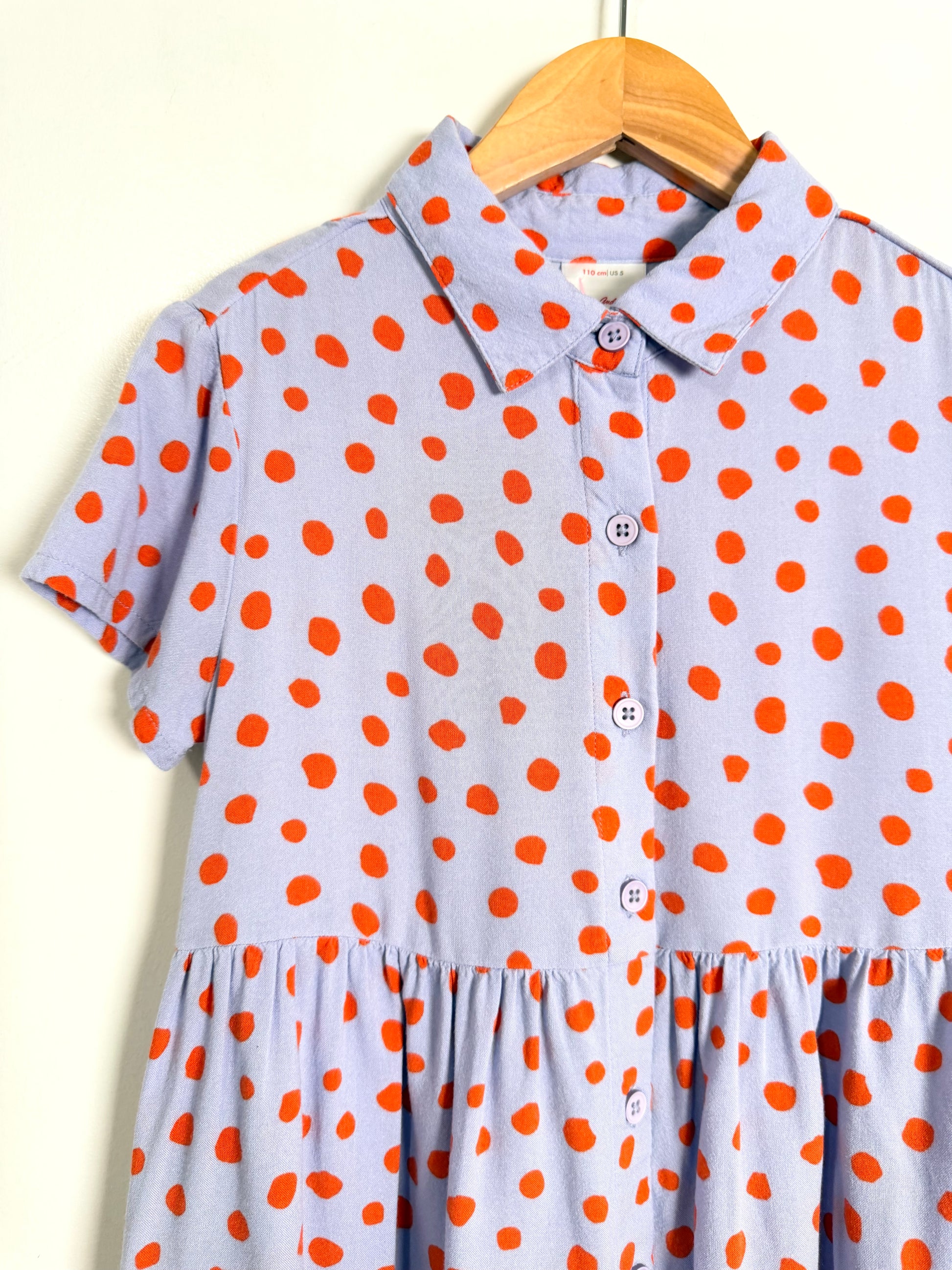 Polka dot dress with orange dots on a wooden hanger against a white background