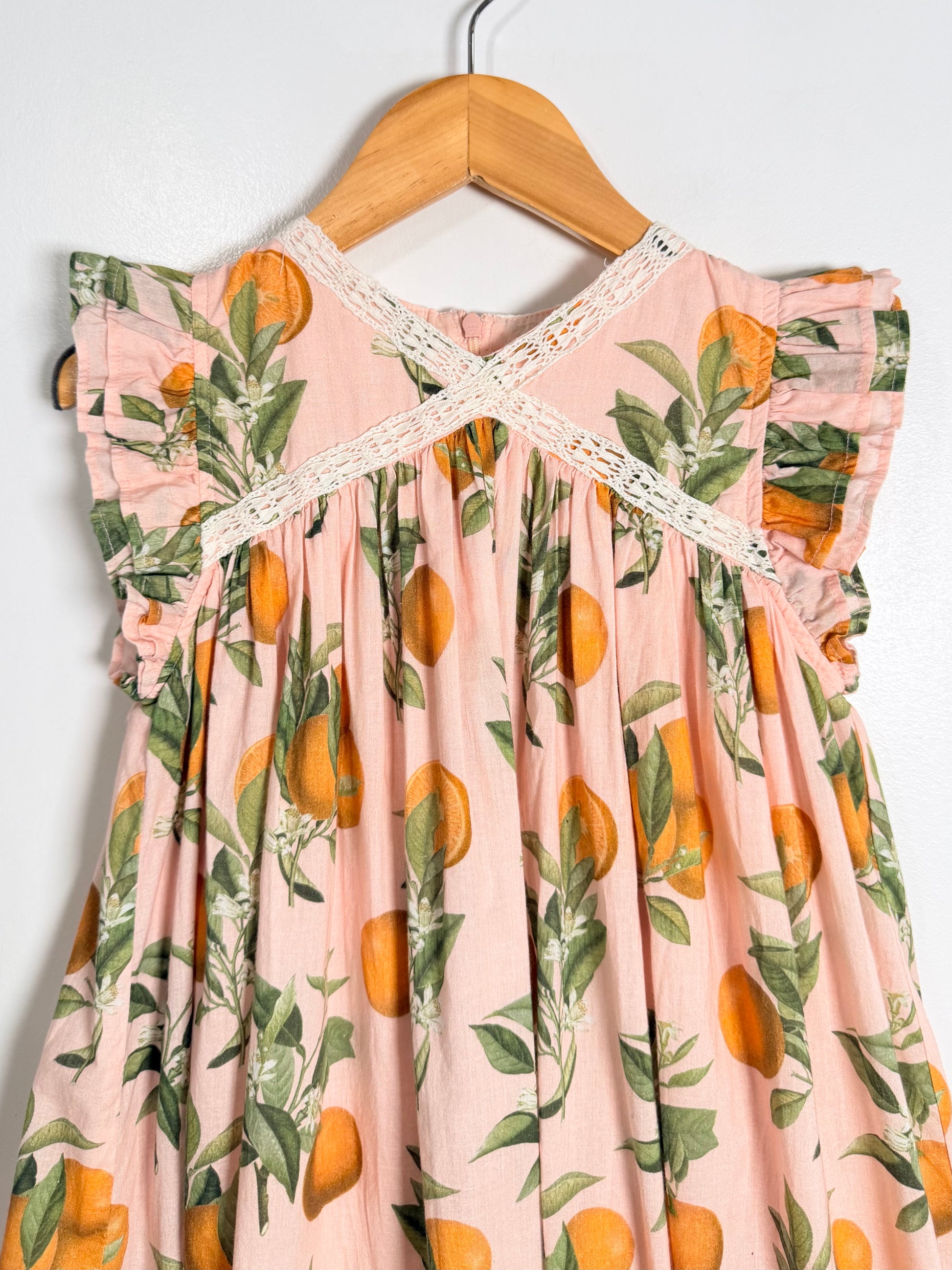 Pink dress with orange and leaf pattern on a wooden hanger against a white background