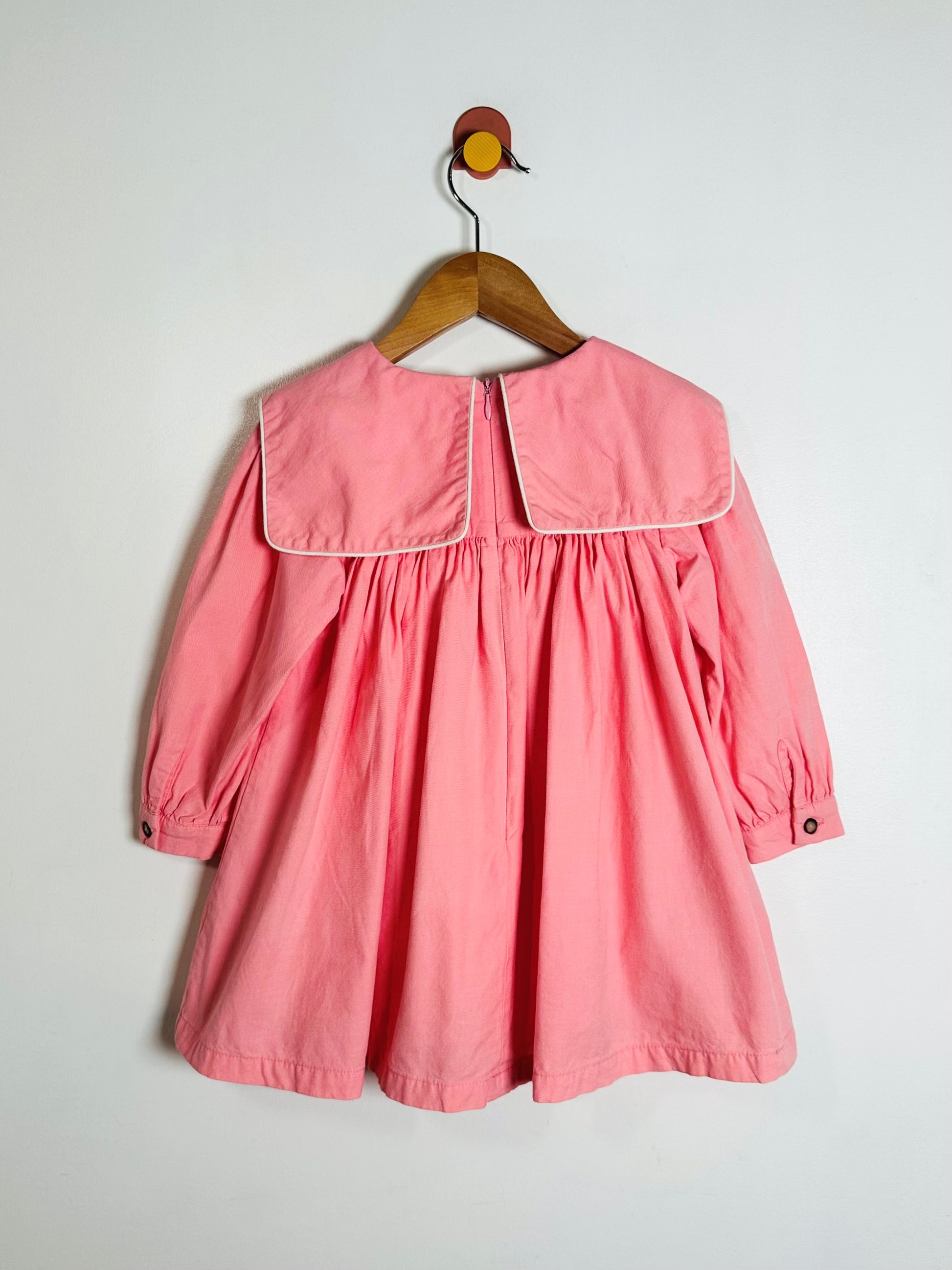 Pink dress on a wooden hanger against a white background