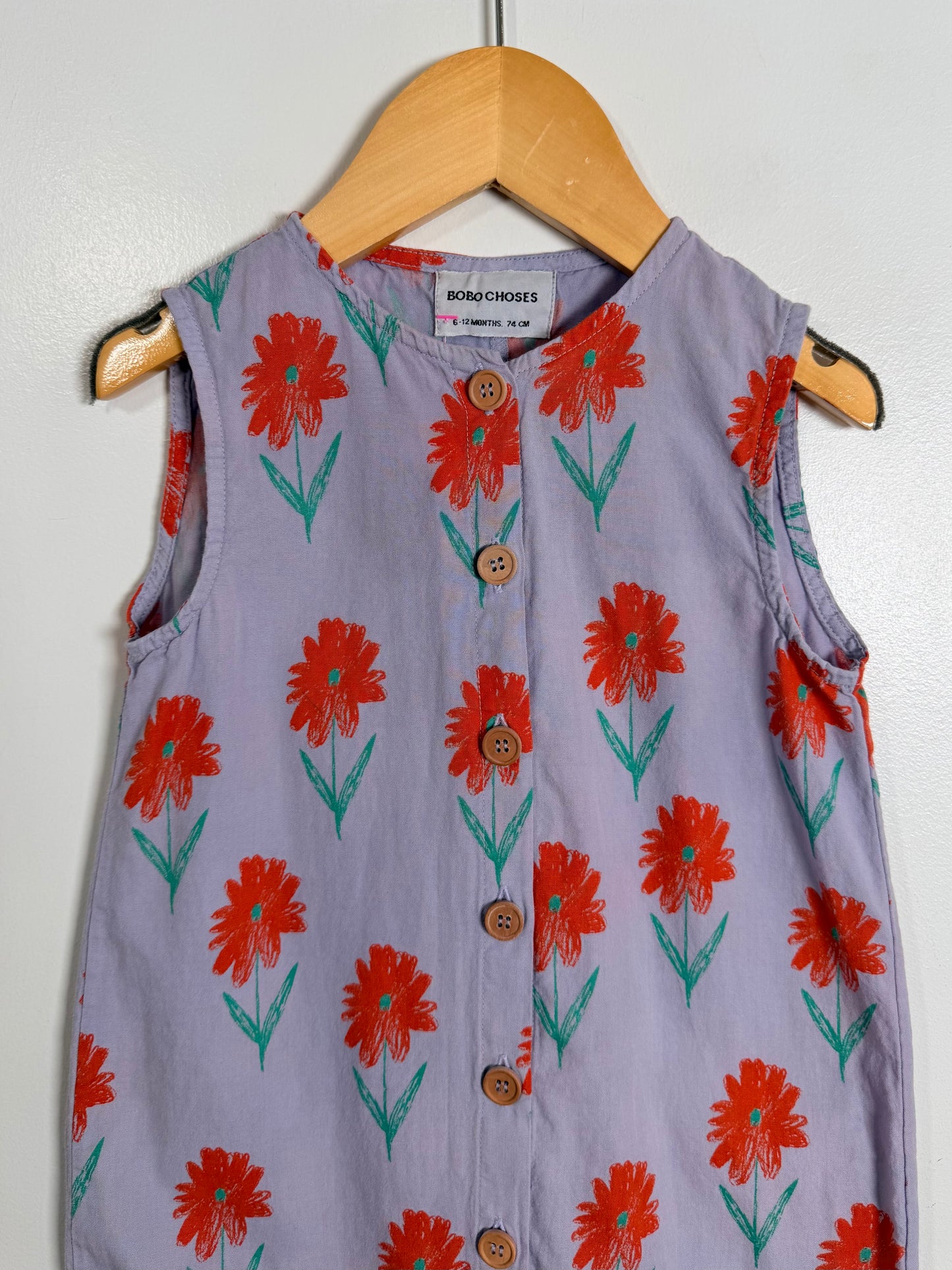 Children's sleeveless dress with red floral pattern on a hanger against a white wall