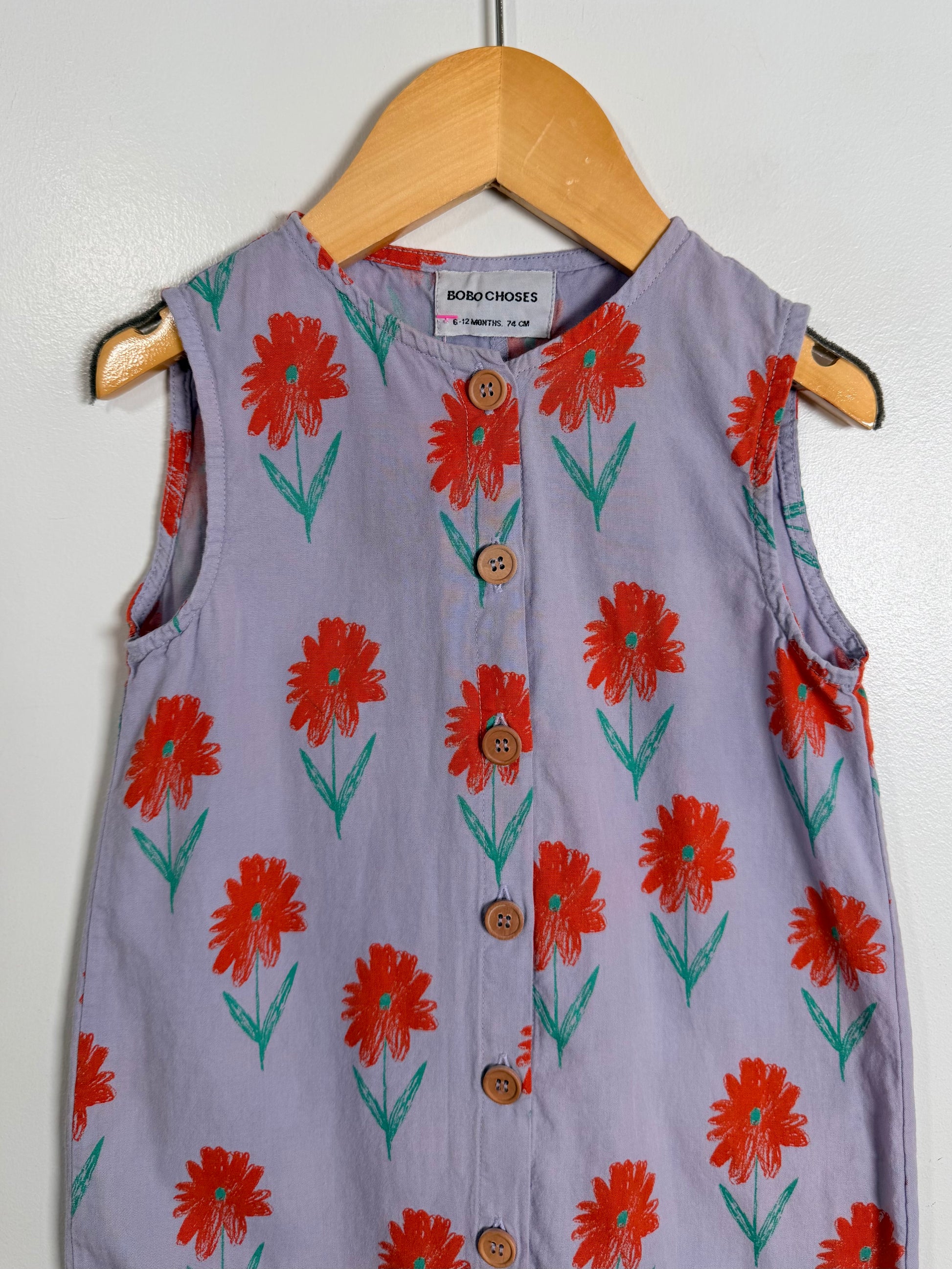 Children's sleeveless dress with red floral pattern on a hanger against a white wall