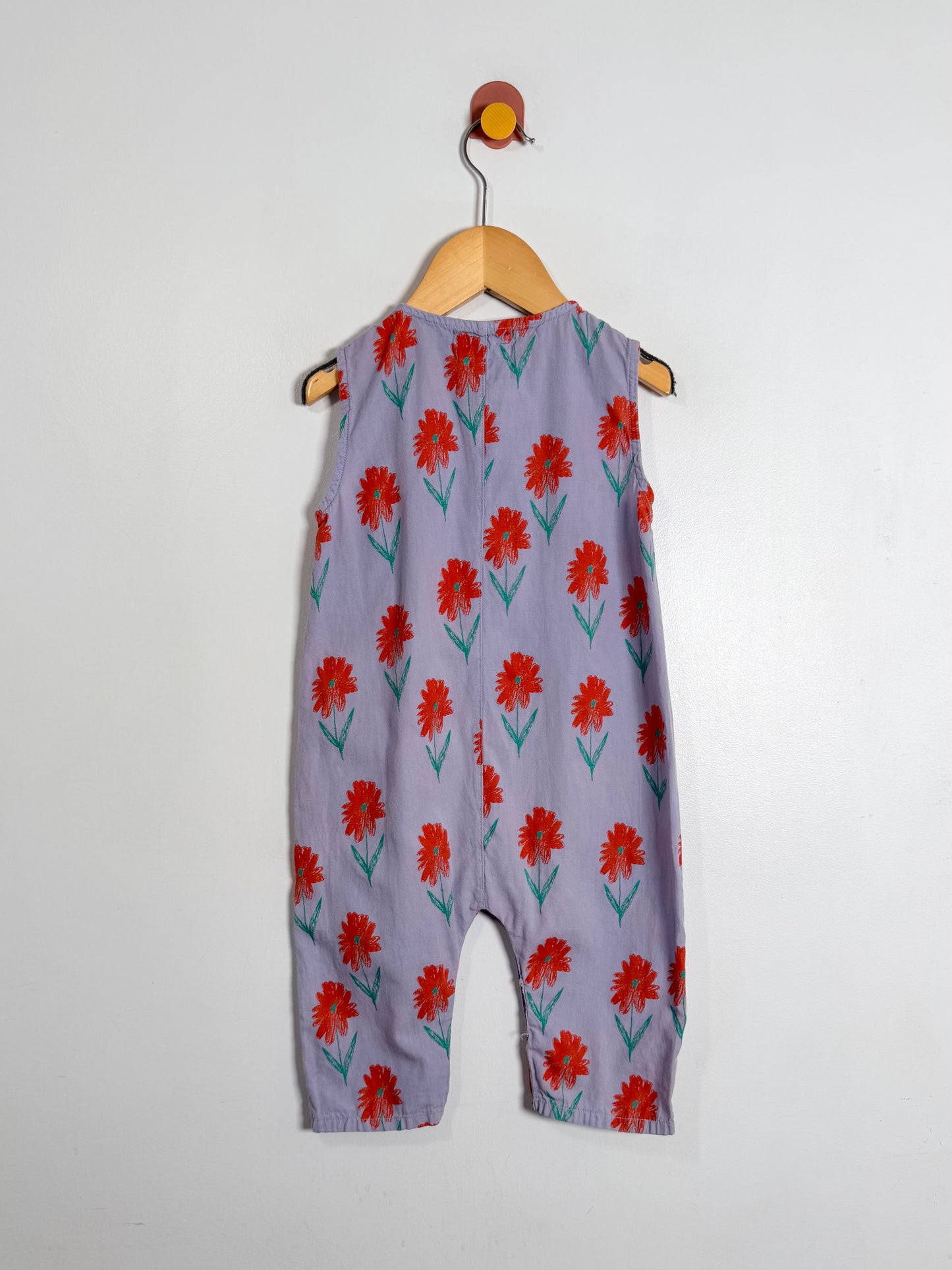 Children's romper with red floral pattern on a wooden hanger against a white background