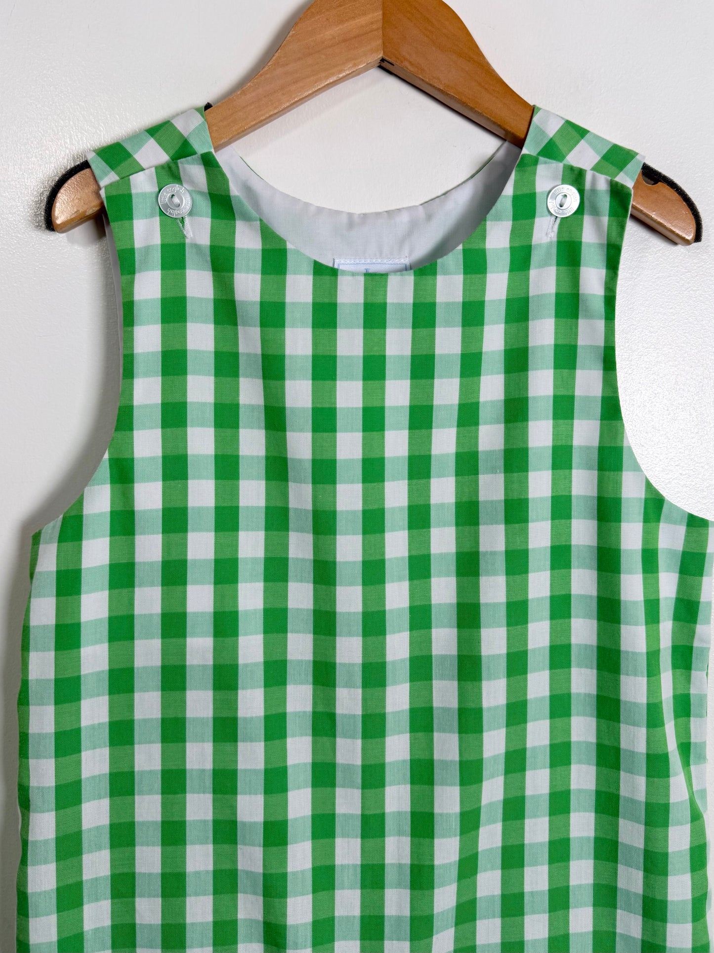 Green and white checkered dress on a wooden hanger against a white background