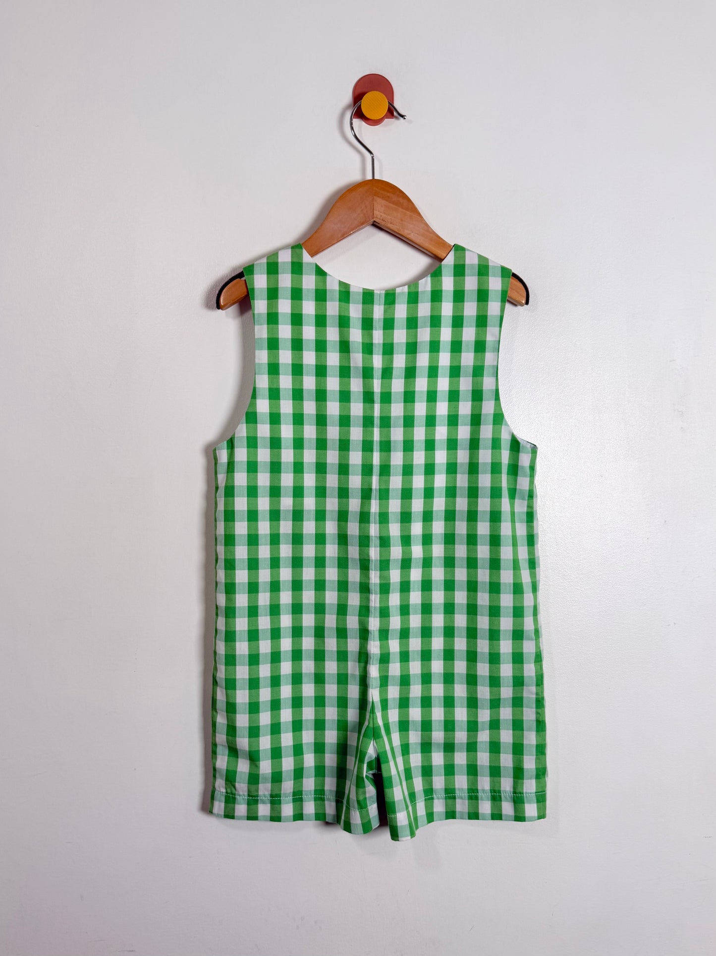 Green checkered romper on a wooden hanger against a white background