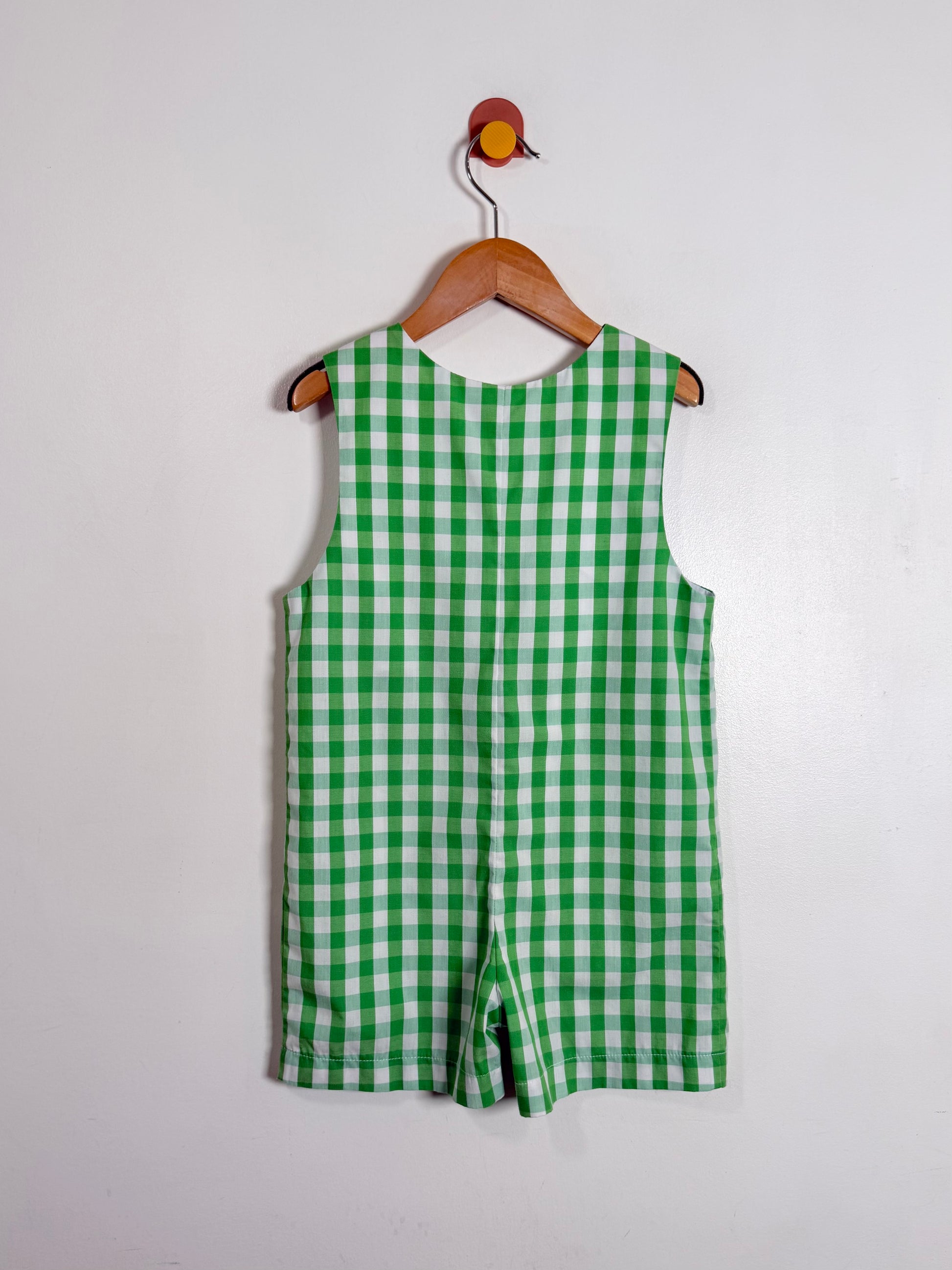 Green checkered romper on a wooden hanger against a white background