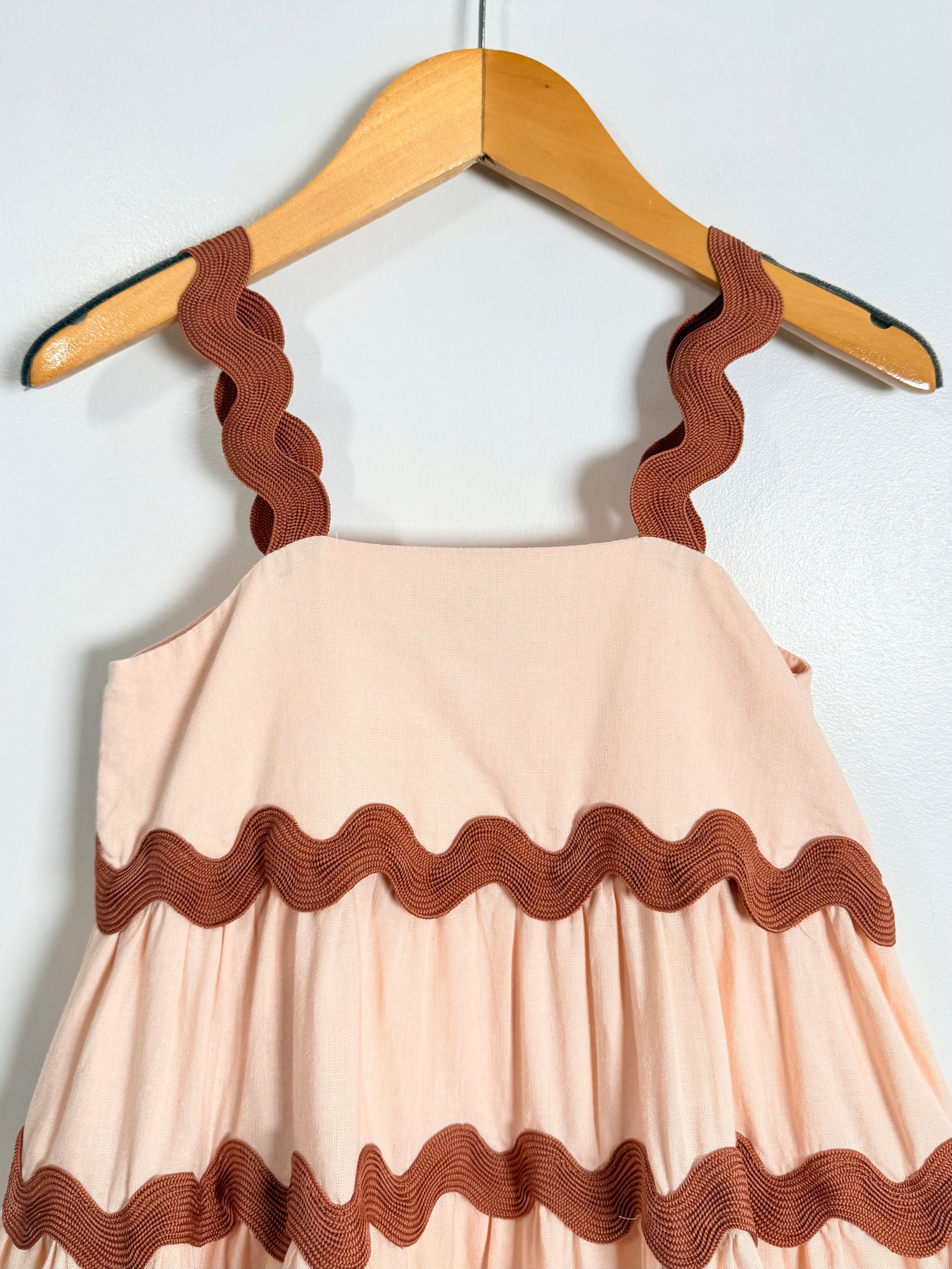 Pink dress with brown ruffled details on a hanger against a white background