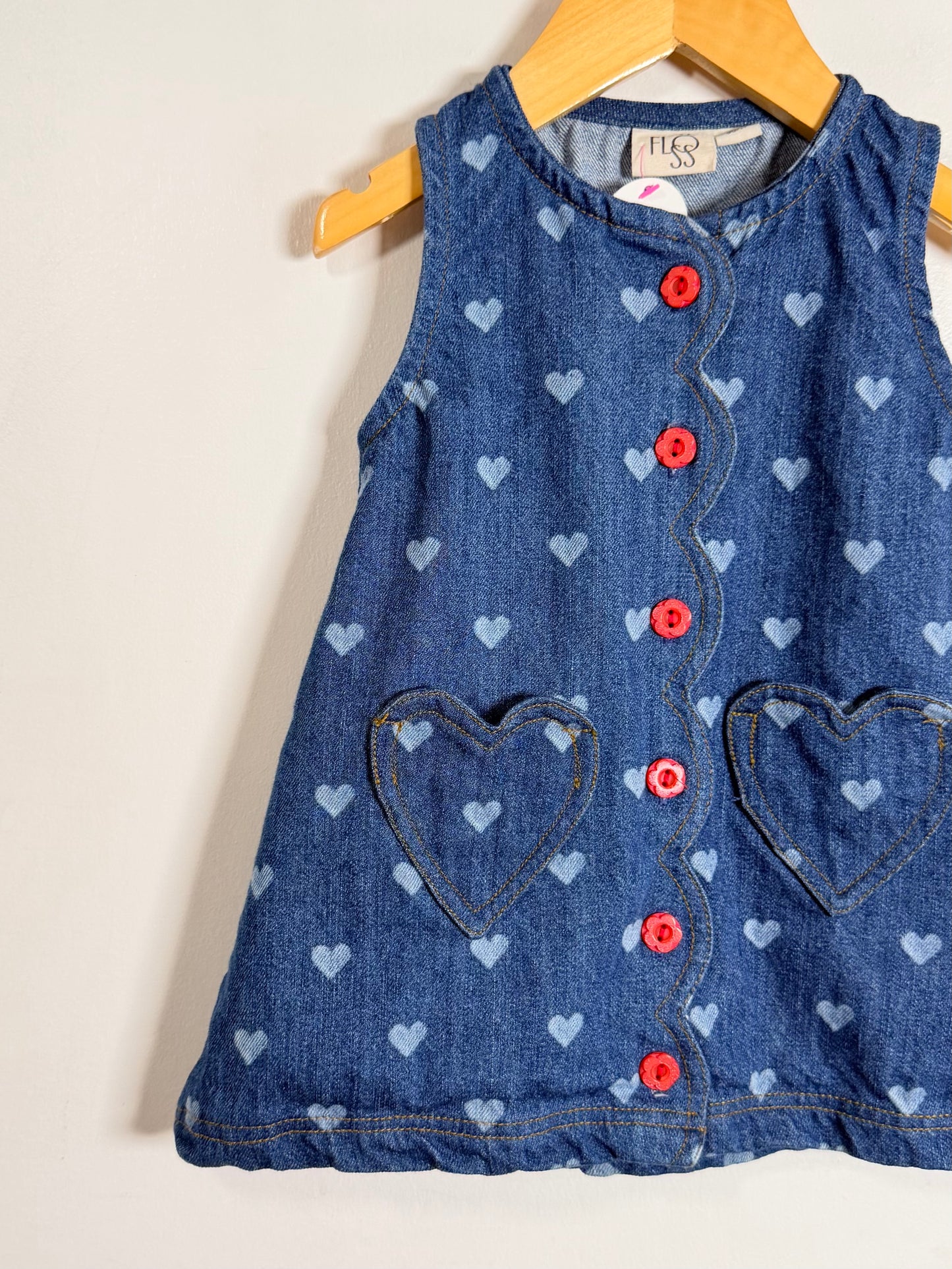 Blue denim dress with heart patterns and red buttons on a hanger