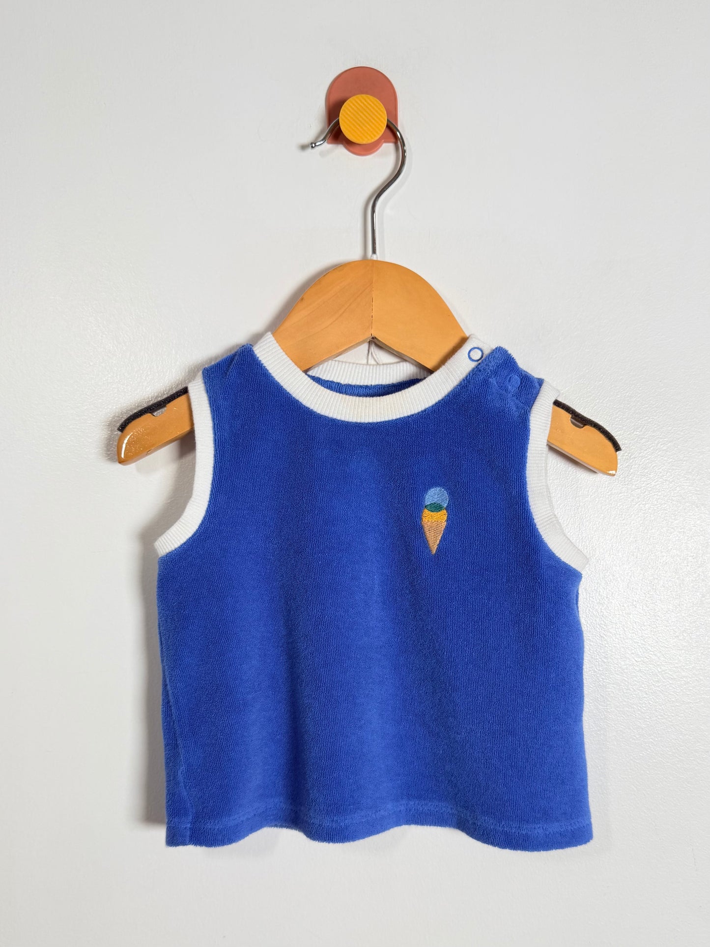 Blue sleeveless shirt with ice cream cone design on a wooden hanger against a white background