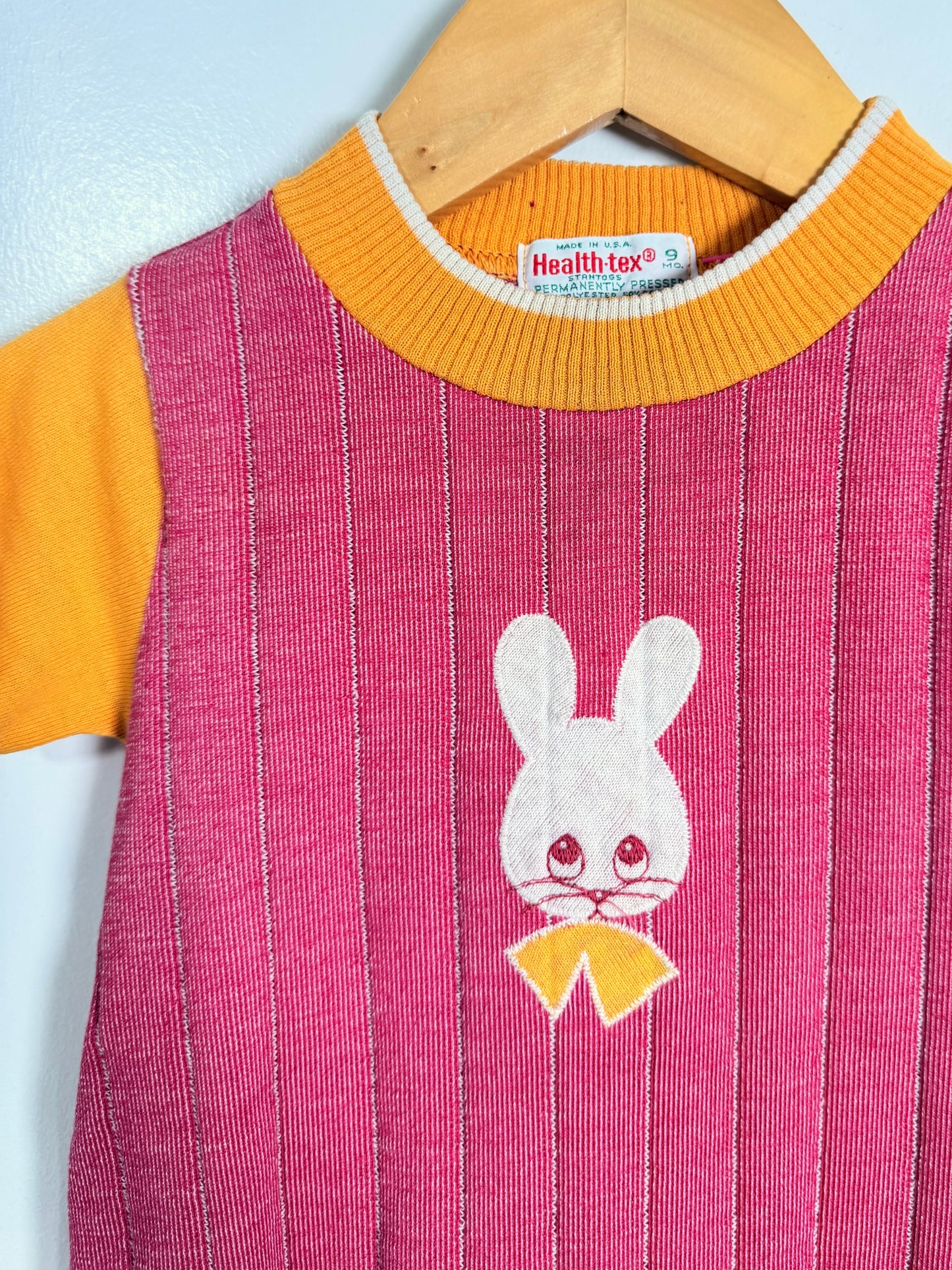 Romper with a white rabbit design and yellow accents on a hanger.