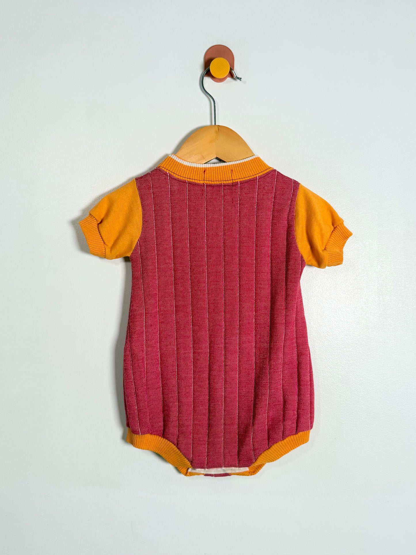 Baby romper with maroon body and yellow sleeves and collar on a hanger against a white background