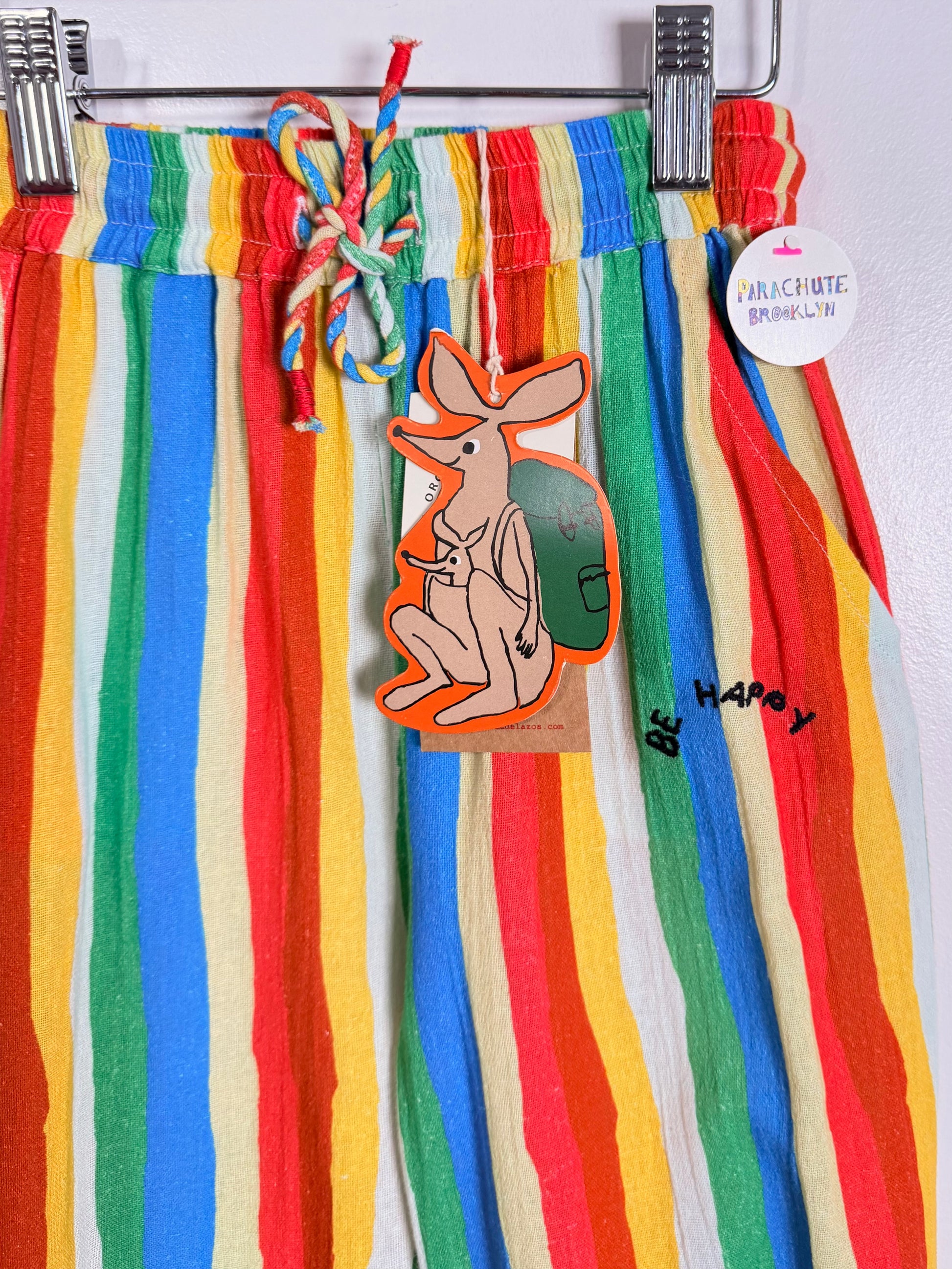 Colorful striped pants with a kangaroo tag and 'Be Happy' text on a white background