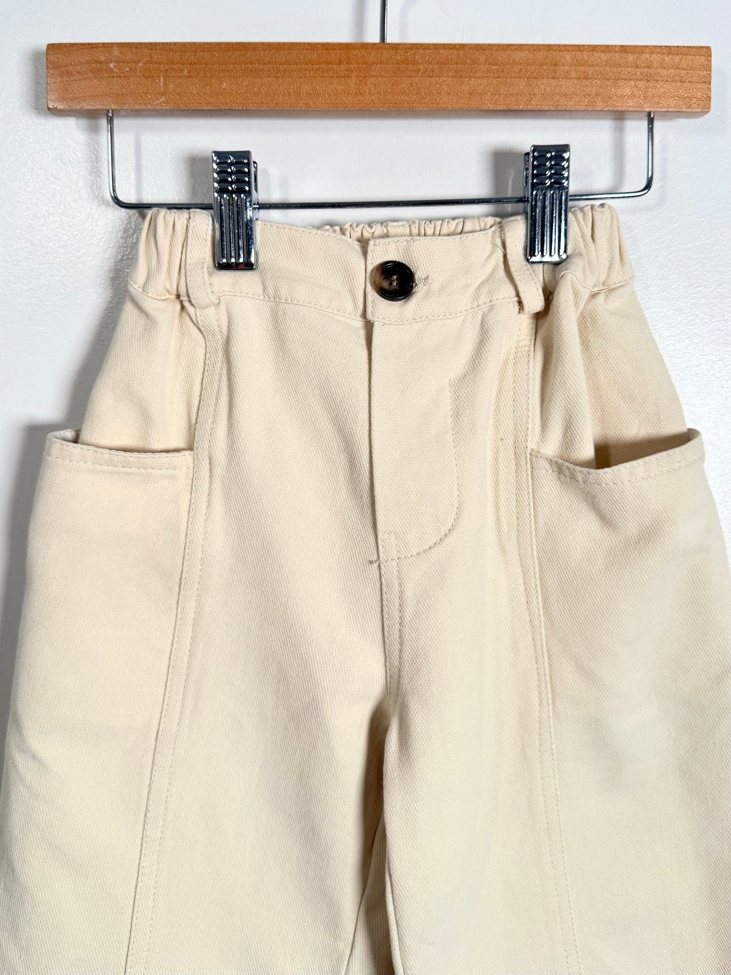 Beige pants hanging on a wooden hanger against a white background