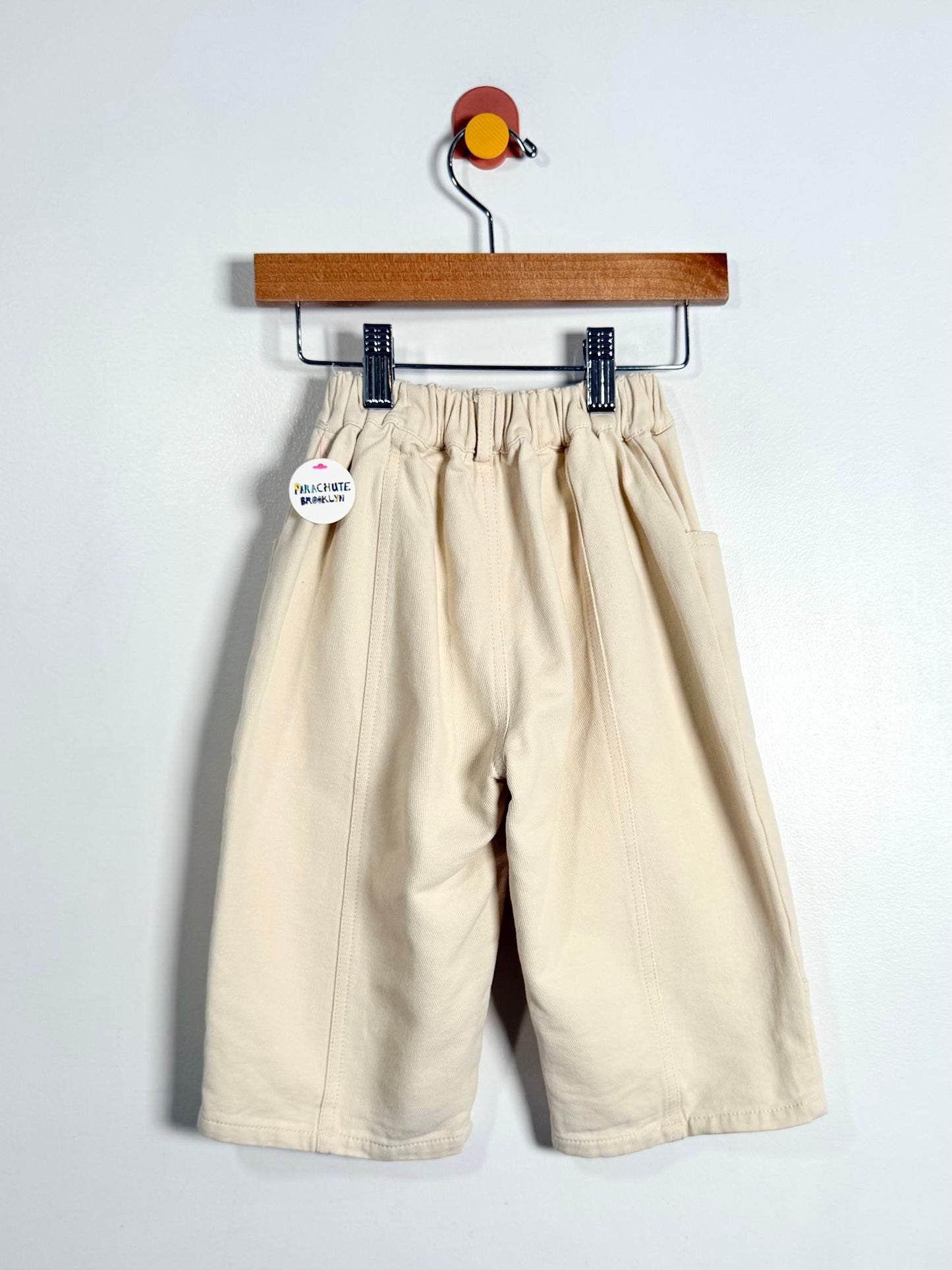 Beige pants hanging on a wooden hanger against a white background