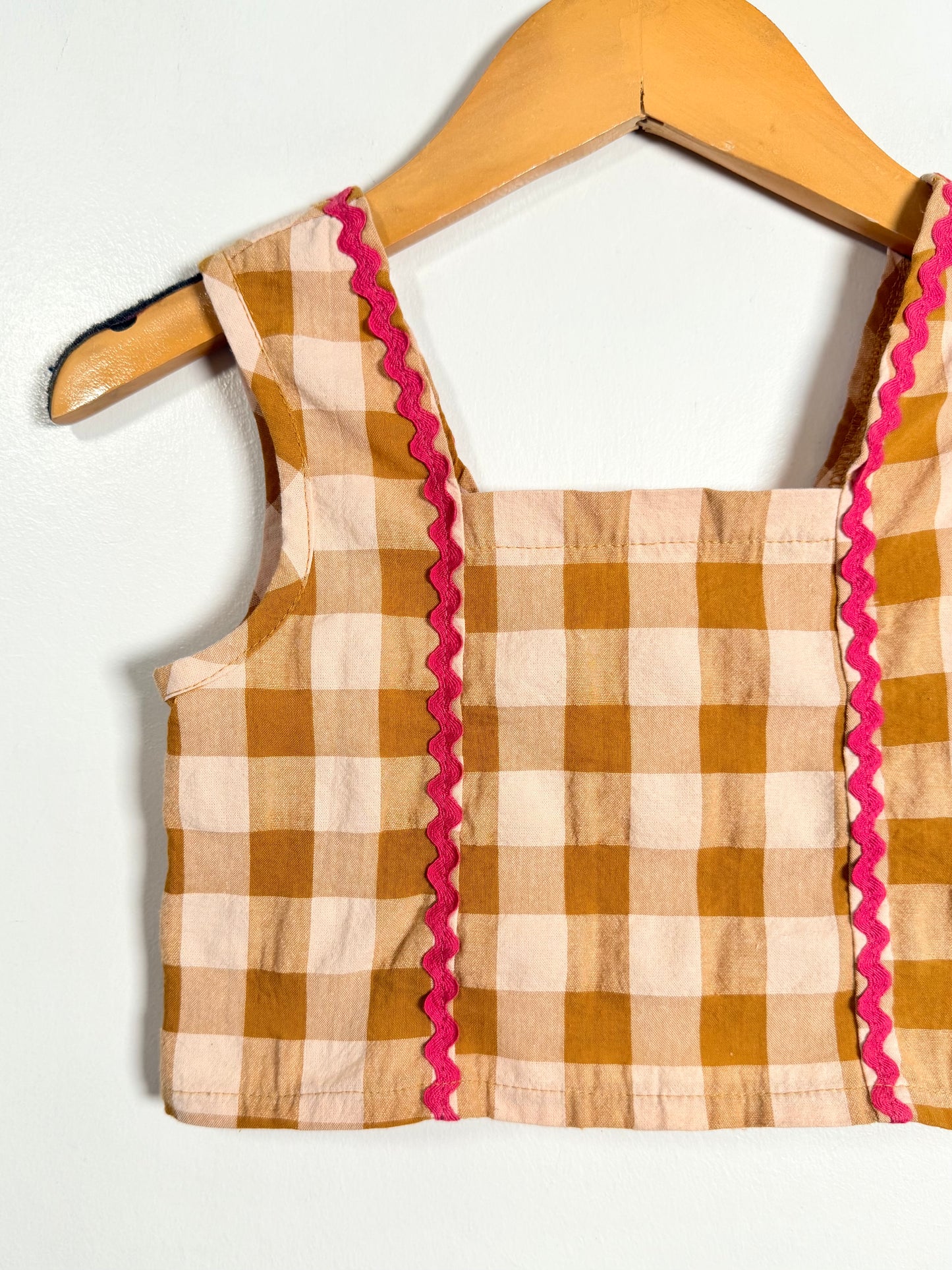 Brown and beige checkered top with pink trim on a wooden hanger against a white background