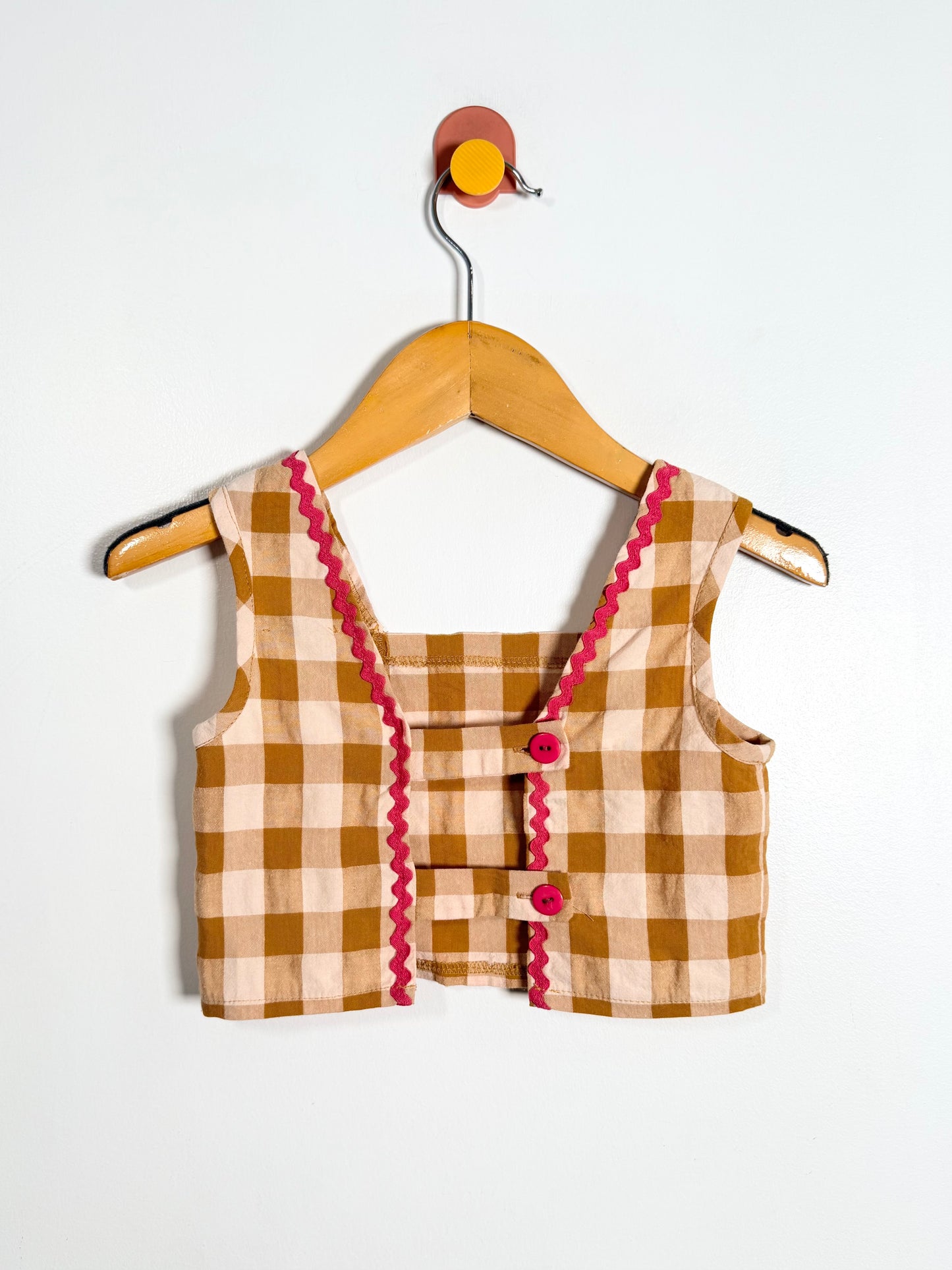 Plaid top with pink trim on a hanger against a white background