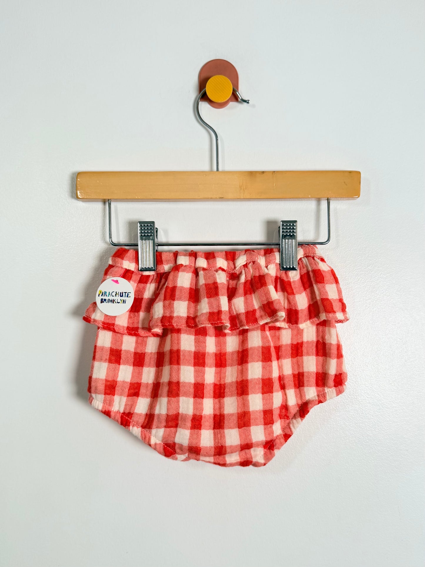 Red and white checkered baby bloomers on a hanger against a white background