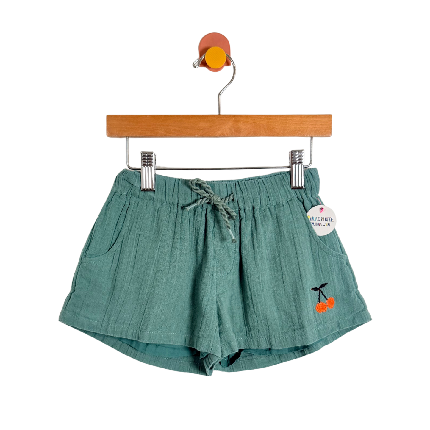 Green shorts with cherry design on a hanger against a white background
