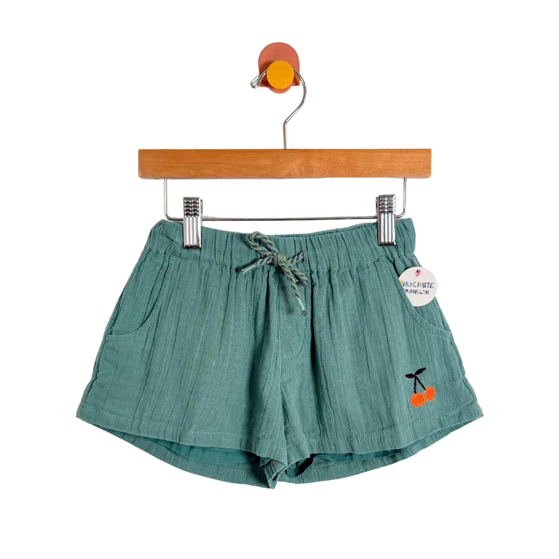 Green shorts with cherry design on a hanger against a white background
