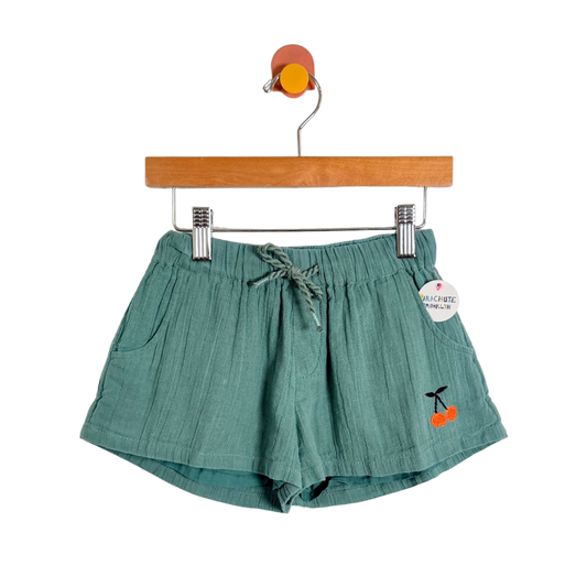 Green shorts with cherry design on a hanger against a white background