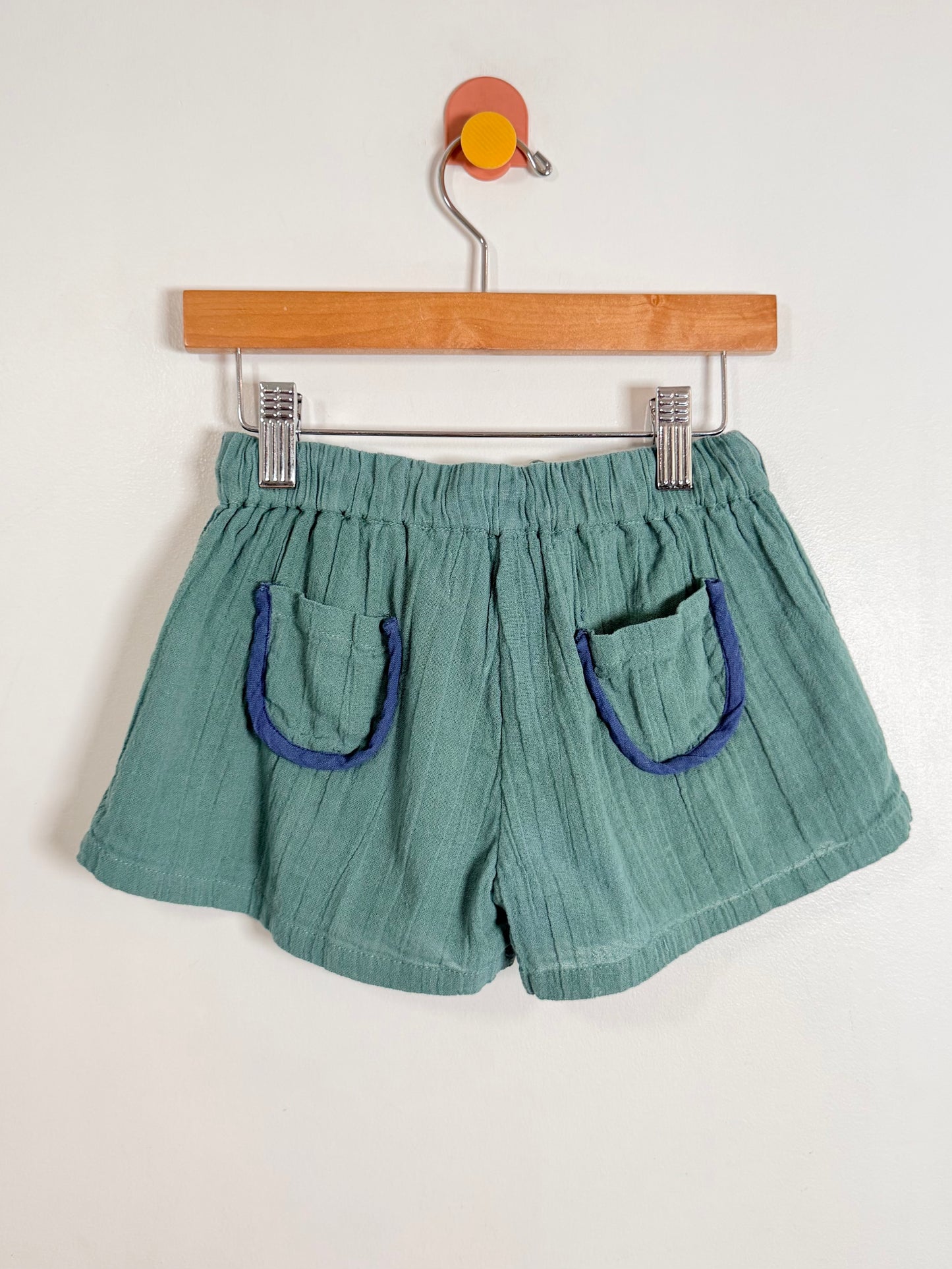 Green shorts with blue pockets on a hanger against a white background