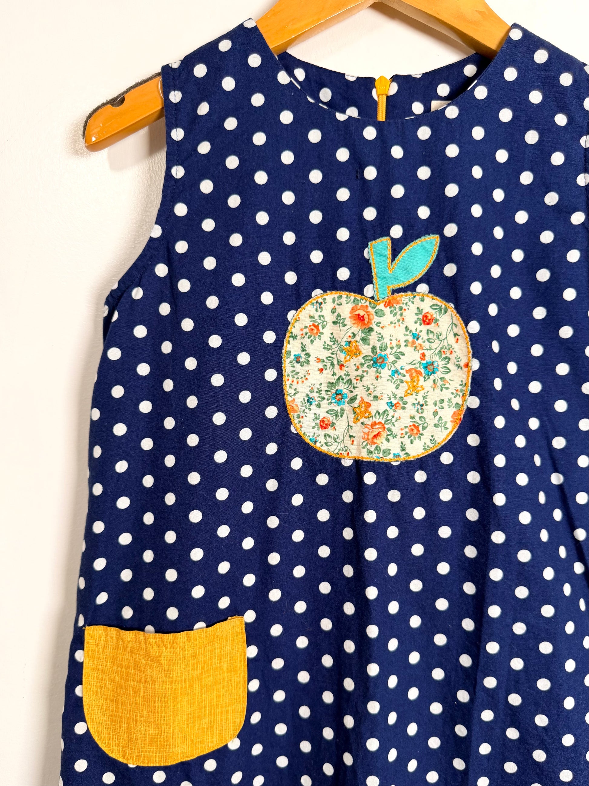 Navy blue dress with white polka dots and a floral apple patch on a hanger.