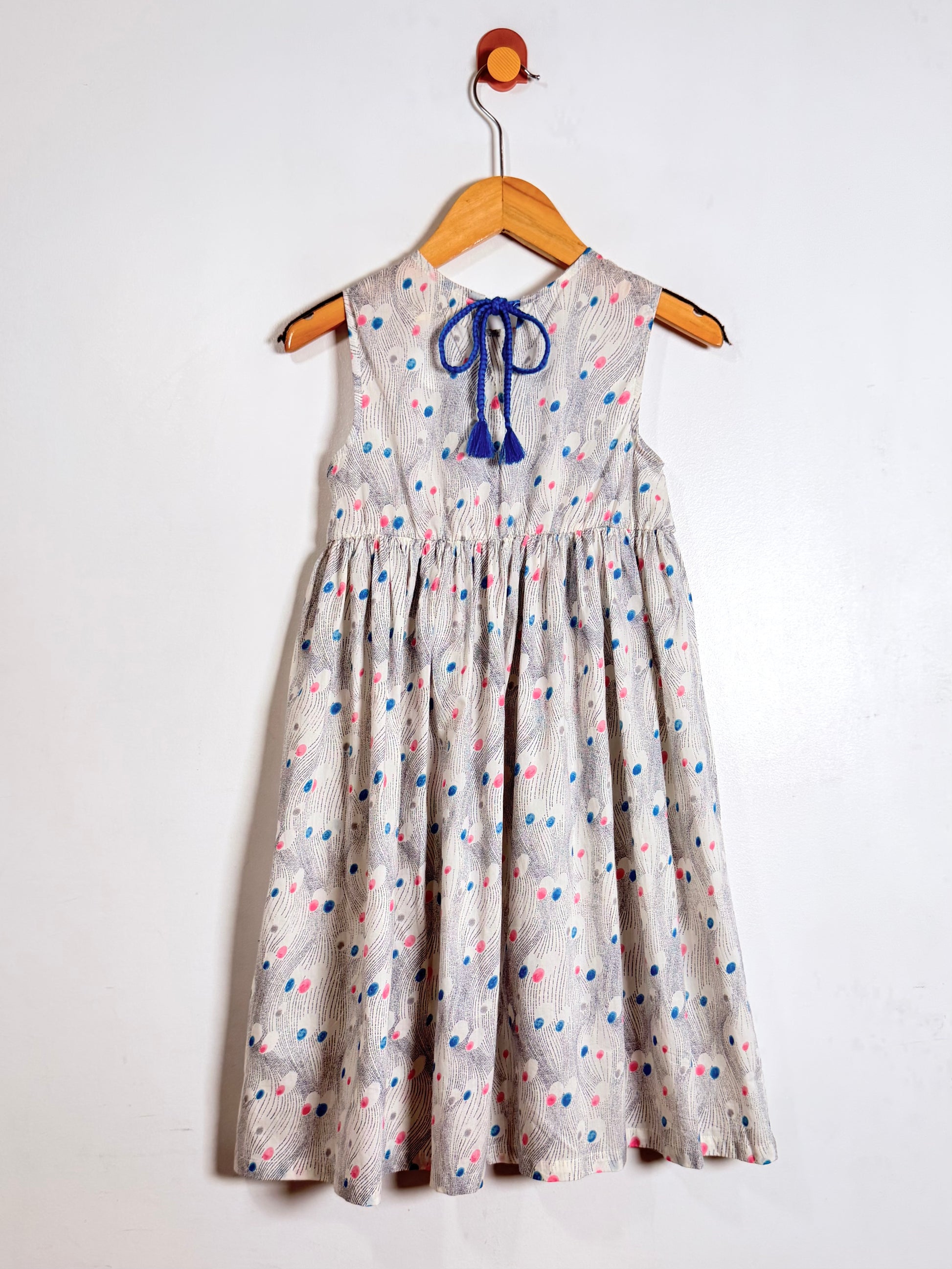 Children's dress with colorful polka dot pattern on a hanger against a white background