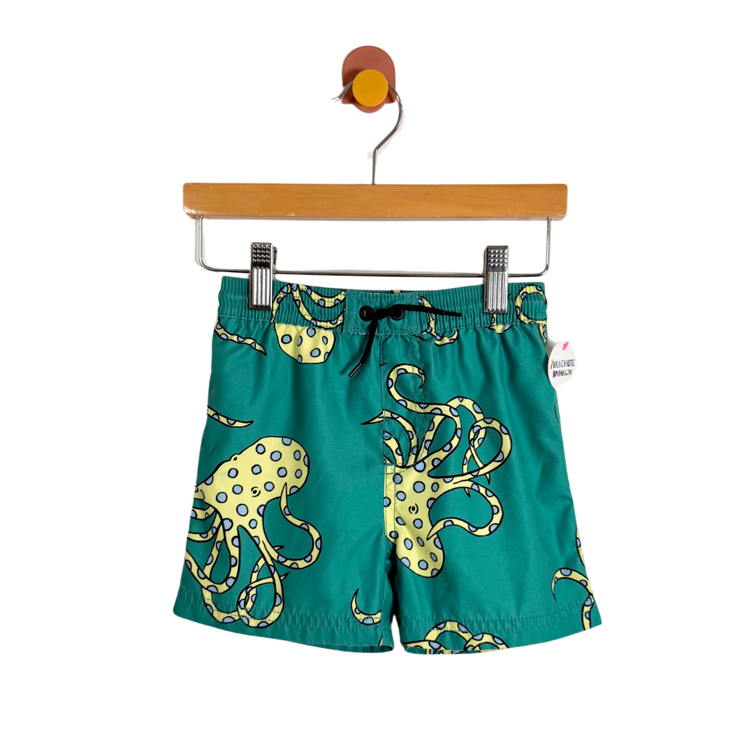 Green shorts with octopus design on a hanger against a white background