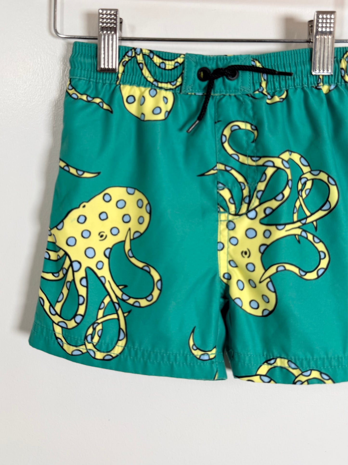 Teal swim shorts with yellow octopus pattern on a white background