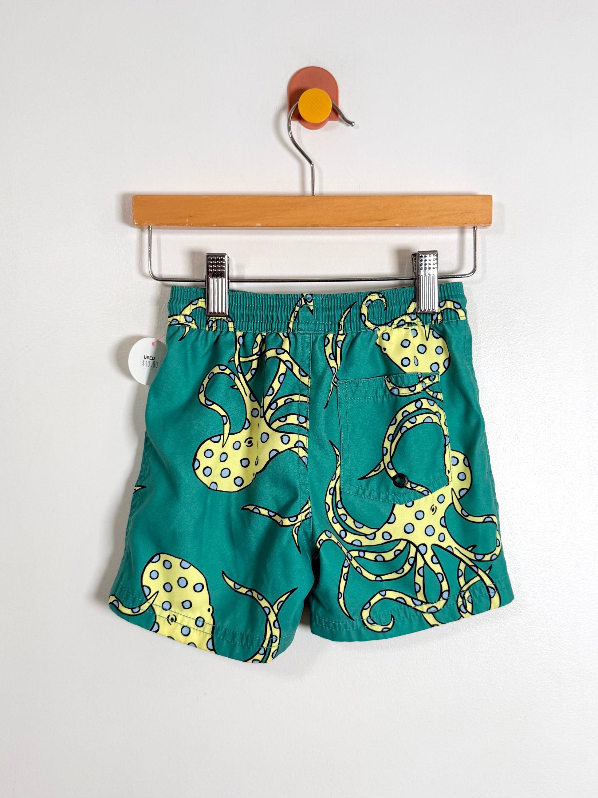 Green shorts with yellow octopus design on a hanger against a white background