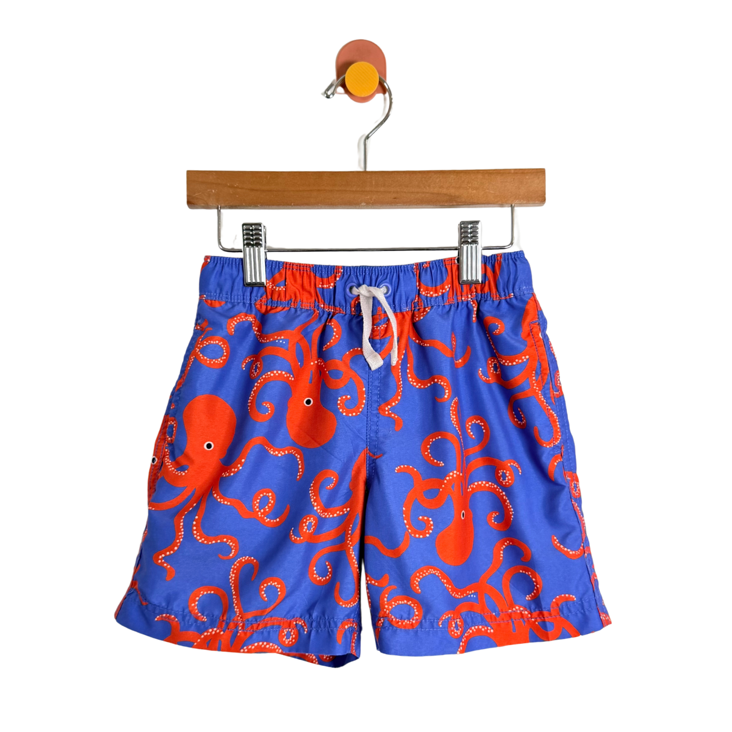 Blue swim shorts with red octopus pattern on a hanger against a white background