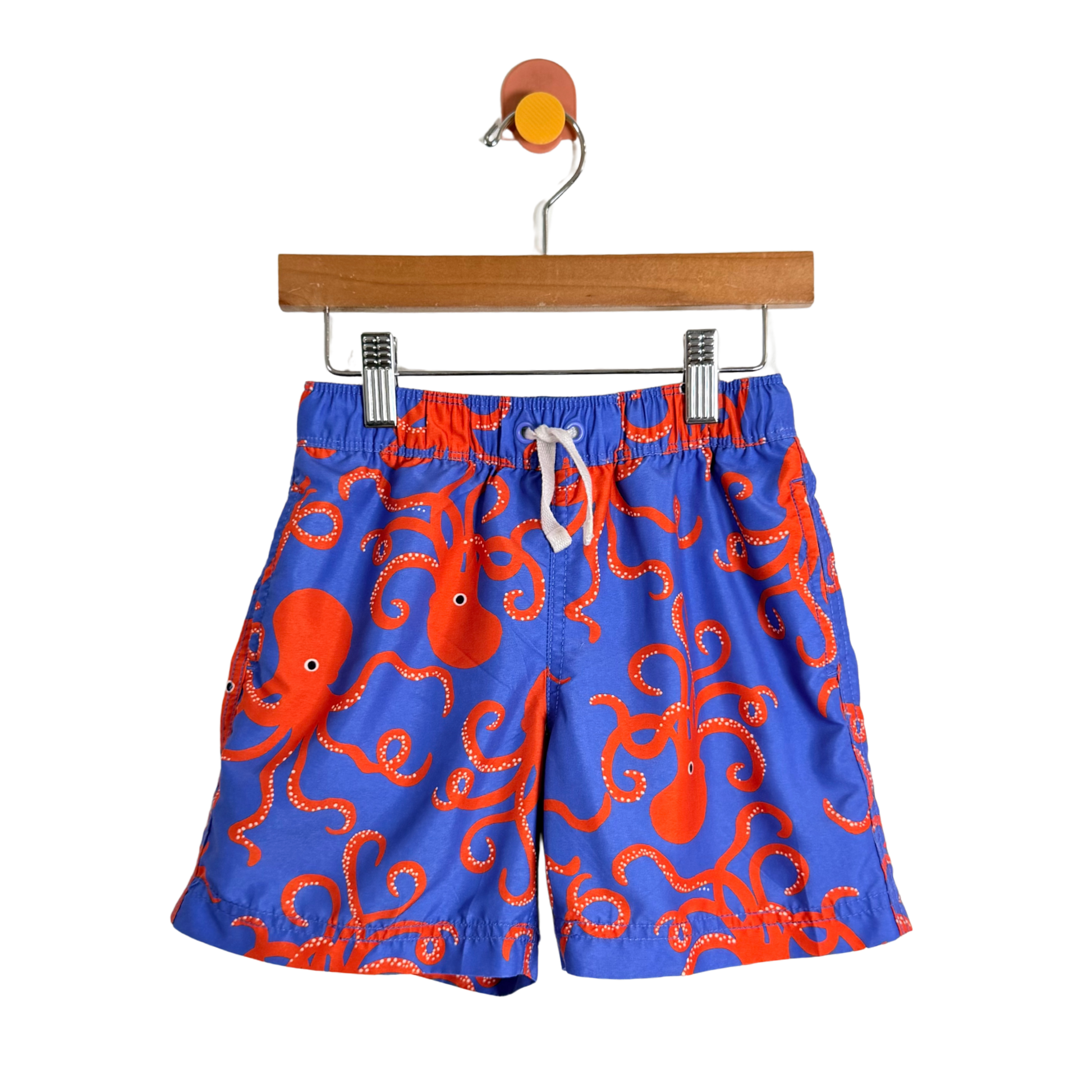 Blue swim shorts with red octopus pattern on a hanger against a white background