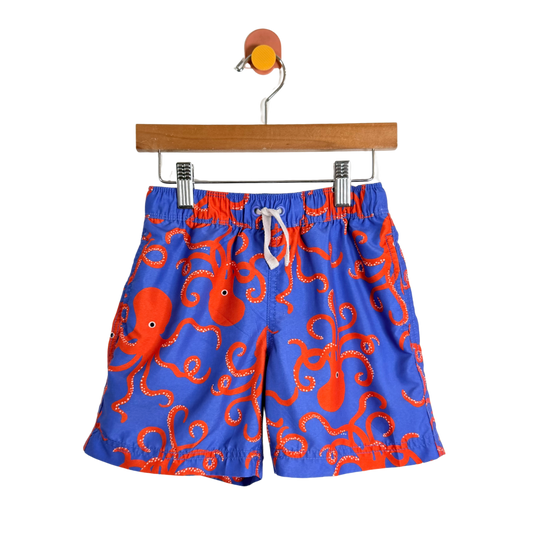 Blue swim shorts with red octopus pattern on a hanger against a white background