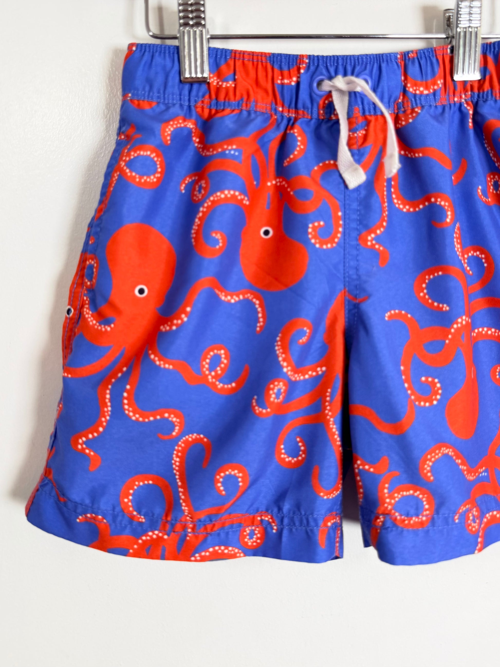 Blue swim shorts with red octopus pattern hanging on a rack.